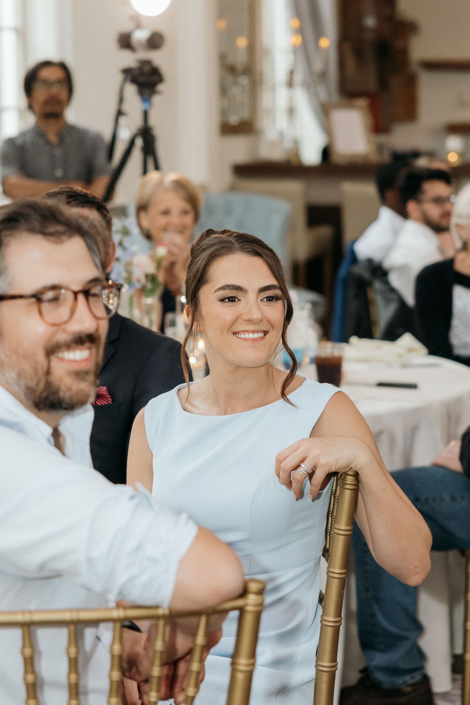 Wedding reception guests seated at tables with gold chiavari chairs.