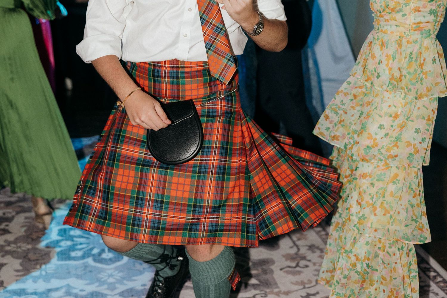 A guest wearing a traditional red and black plaid kilt at a wedding reception.