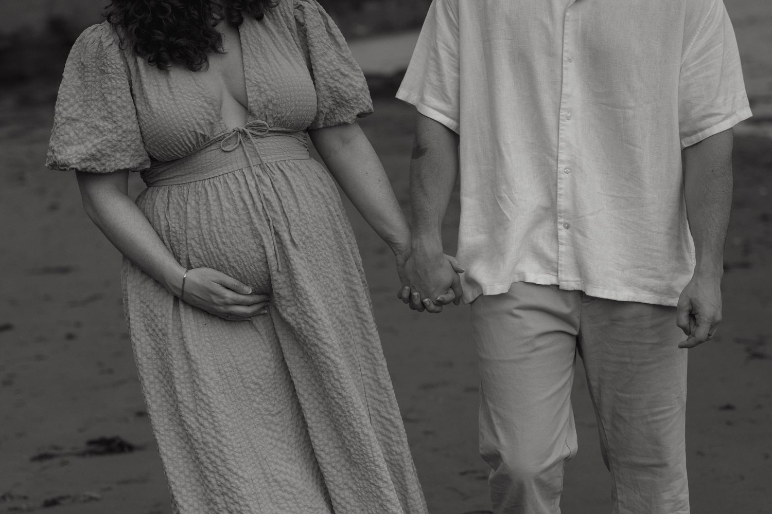 A couple stands close together on a beach during an outdoor photoshoot.