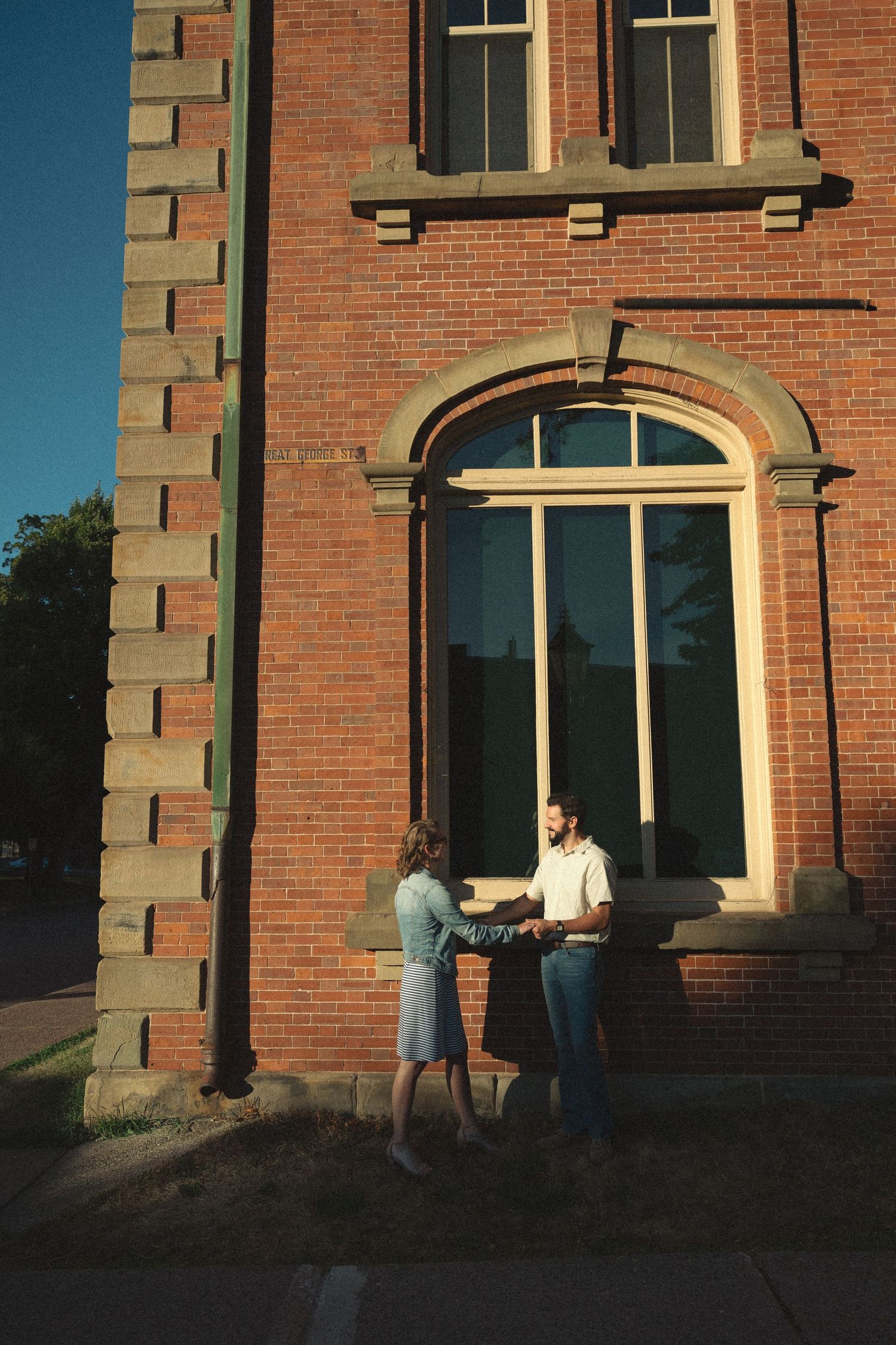 Two figures stand in dramatic evening light against a historic brick building entrance.