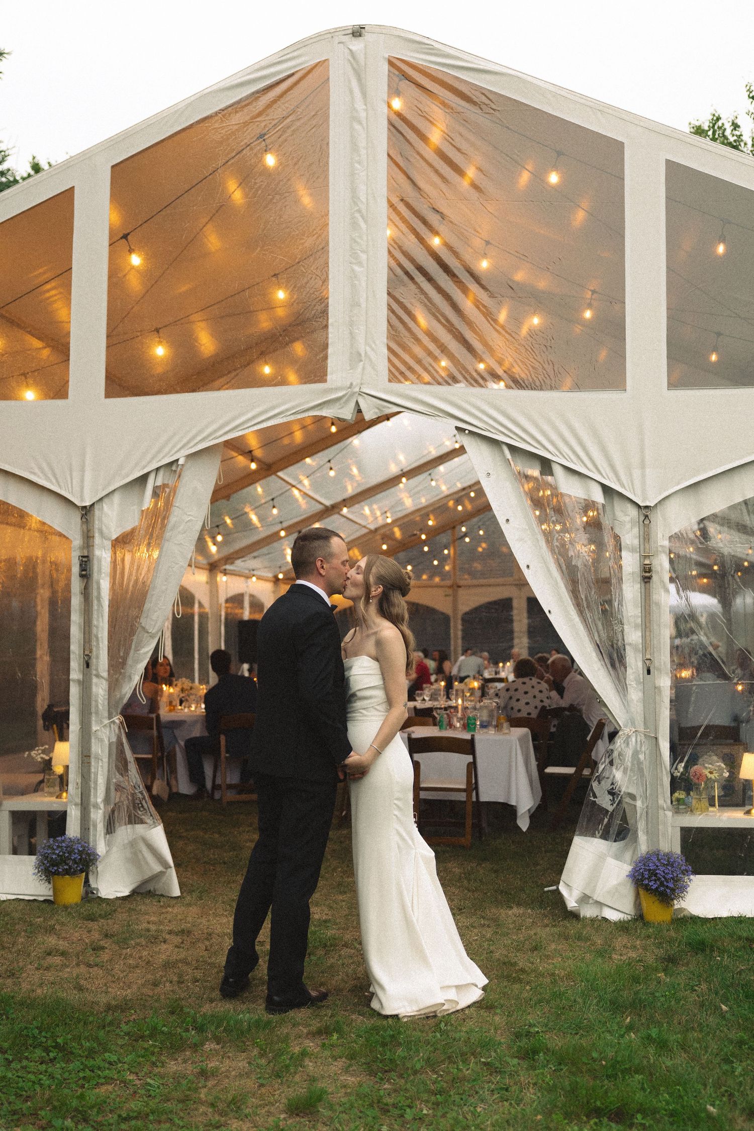 Bride and groom share first dance under elegant clear tent with string lights at outdoor evening reception.