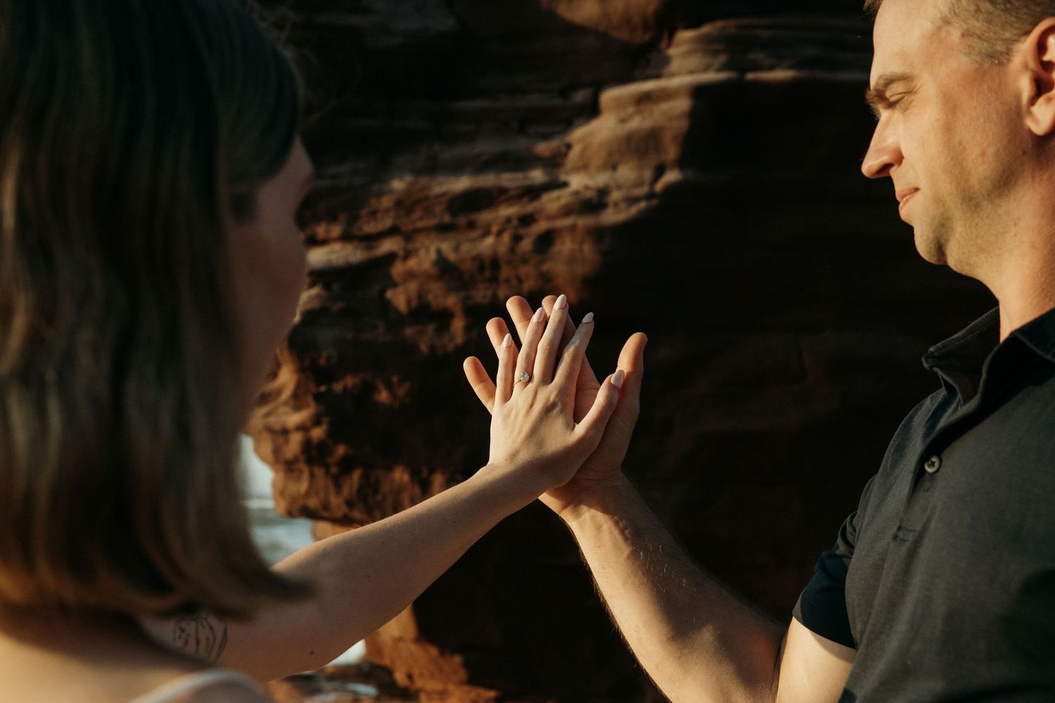 Close-up of hands reaching toward each other against rocky cliff background.