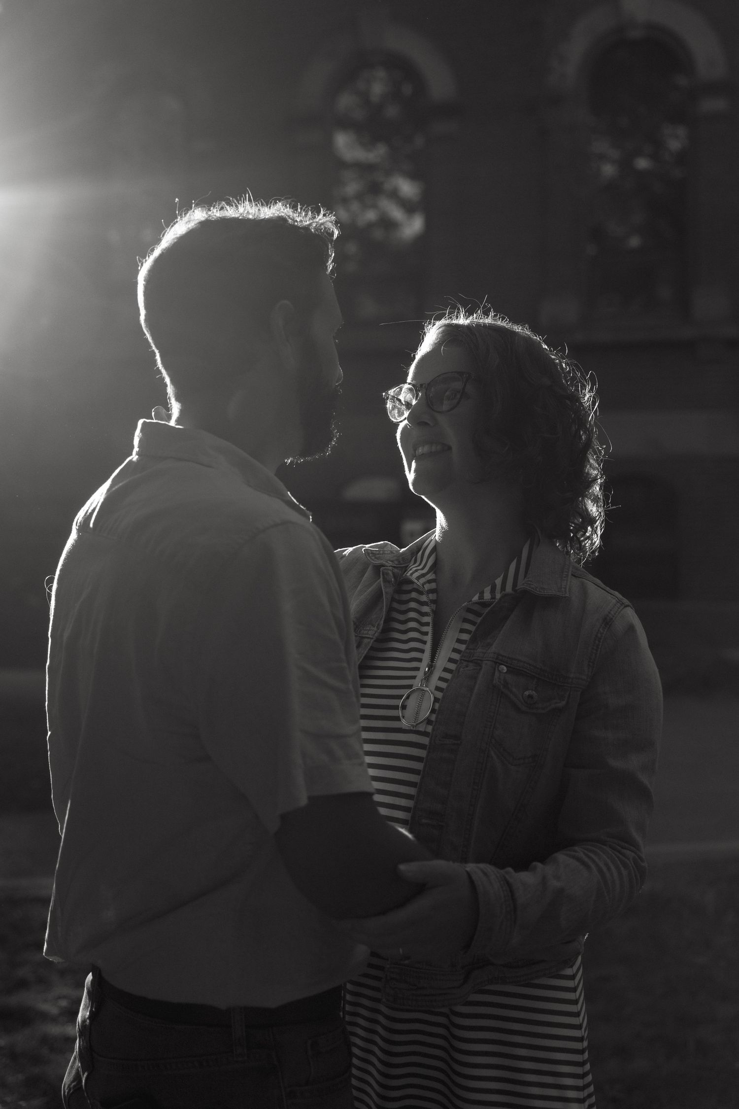 Silhouetted figures embrace in dramatic backlit black and white photography.