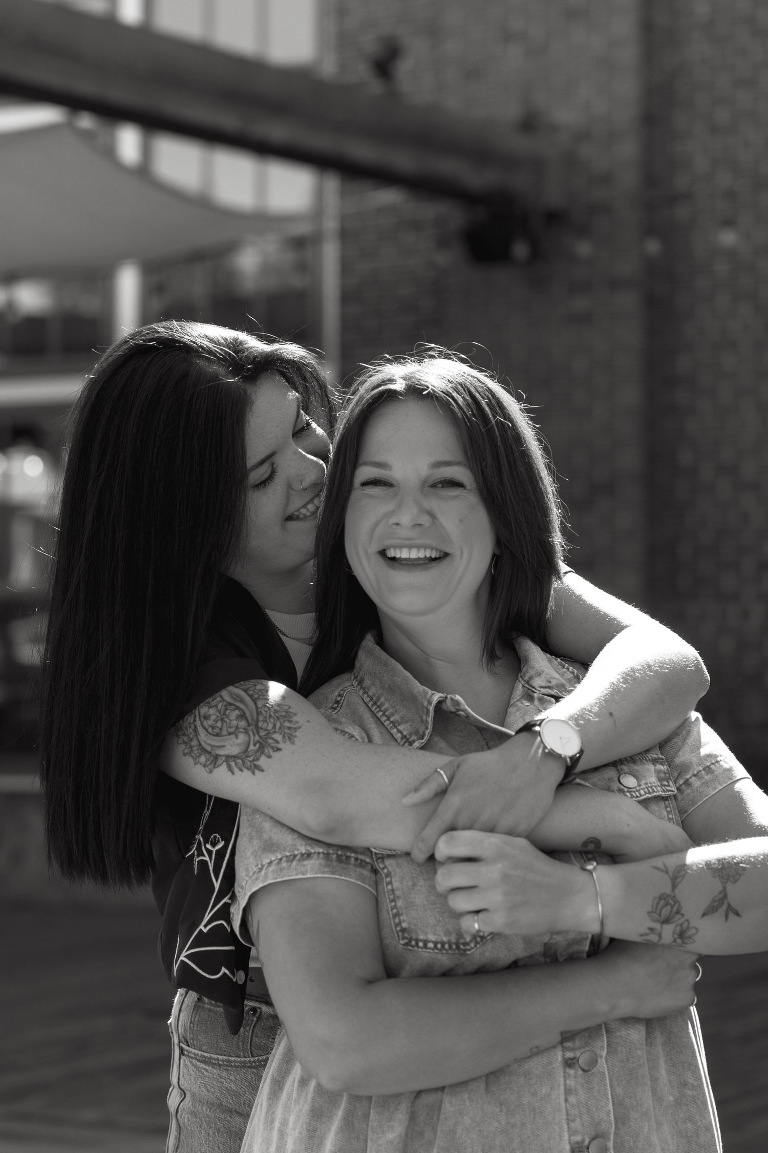 Two people sharing an affectionate moment while laughing outside a brick building.