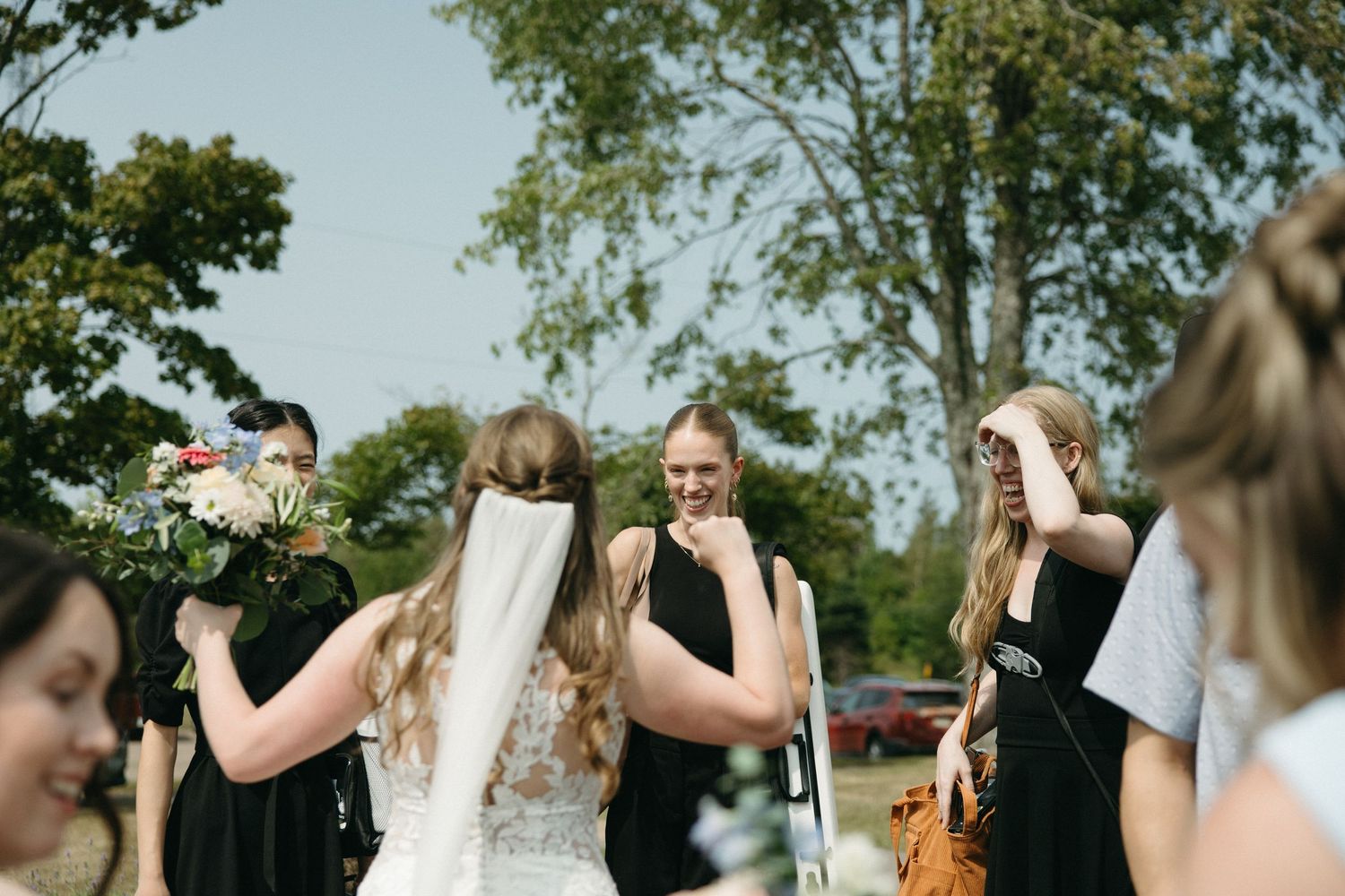 Wedding guests gather outdoors under green trees for celebration.