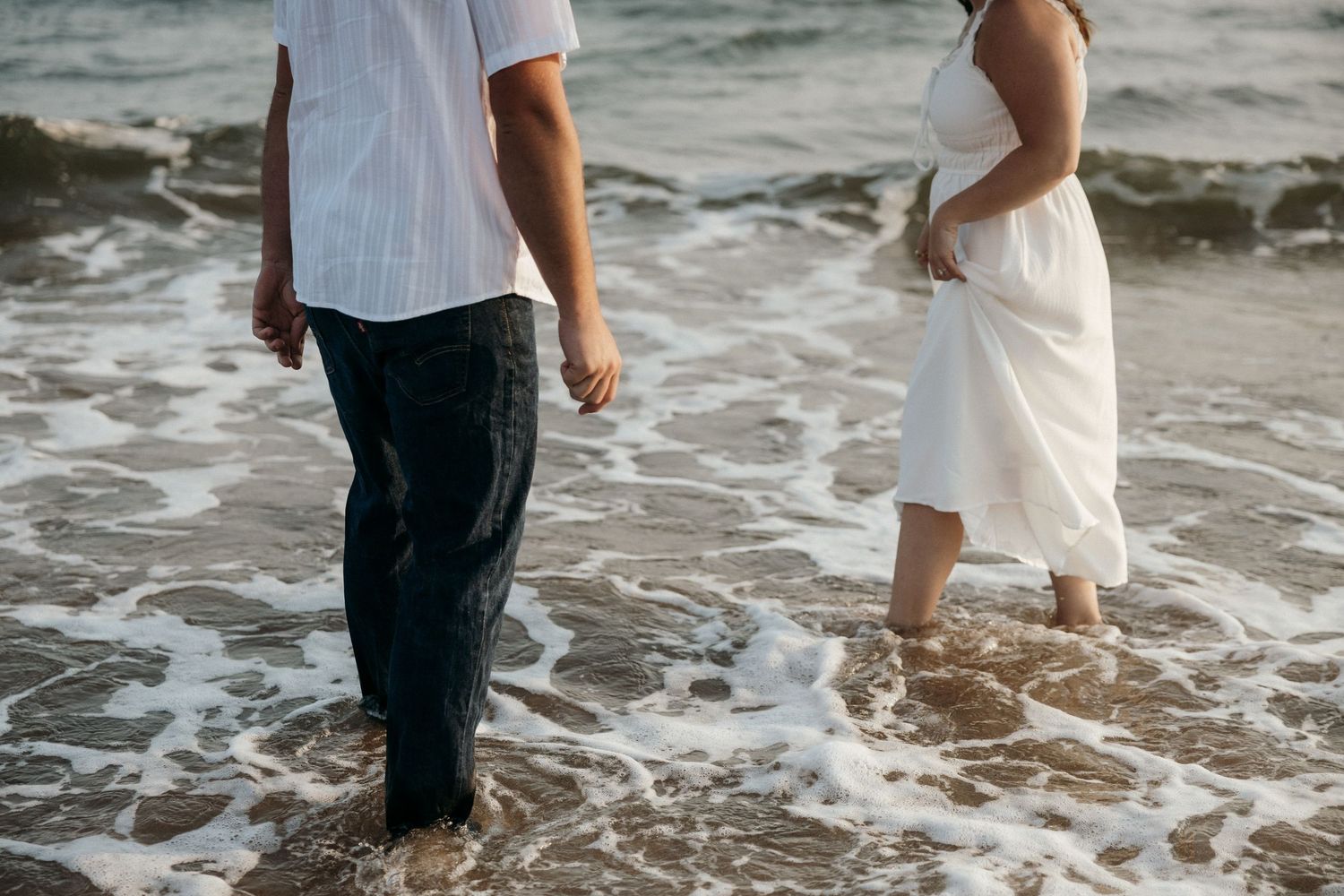 A couple splashes in the ocean waves wearing white and dark clothing.