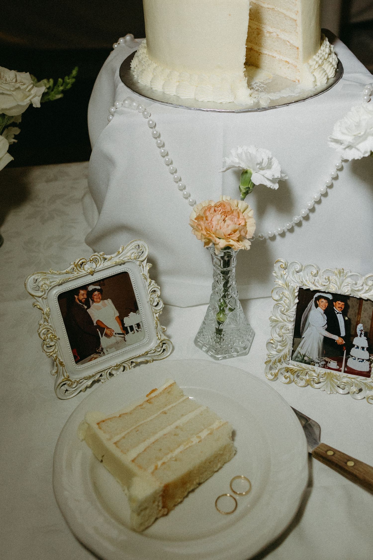 Wedding cake display with framed photos, rings, and peach floral accents.