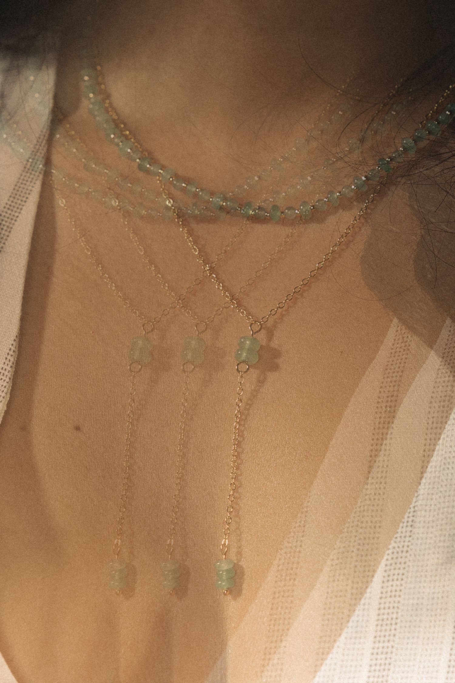 Delicate layered necklaces with crystal pendants draped against sheer fabric in soft lighting.