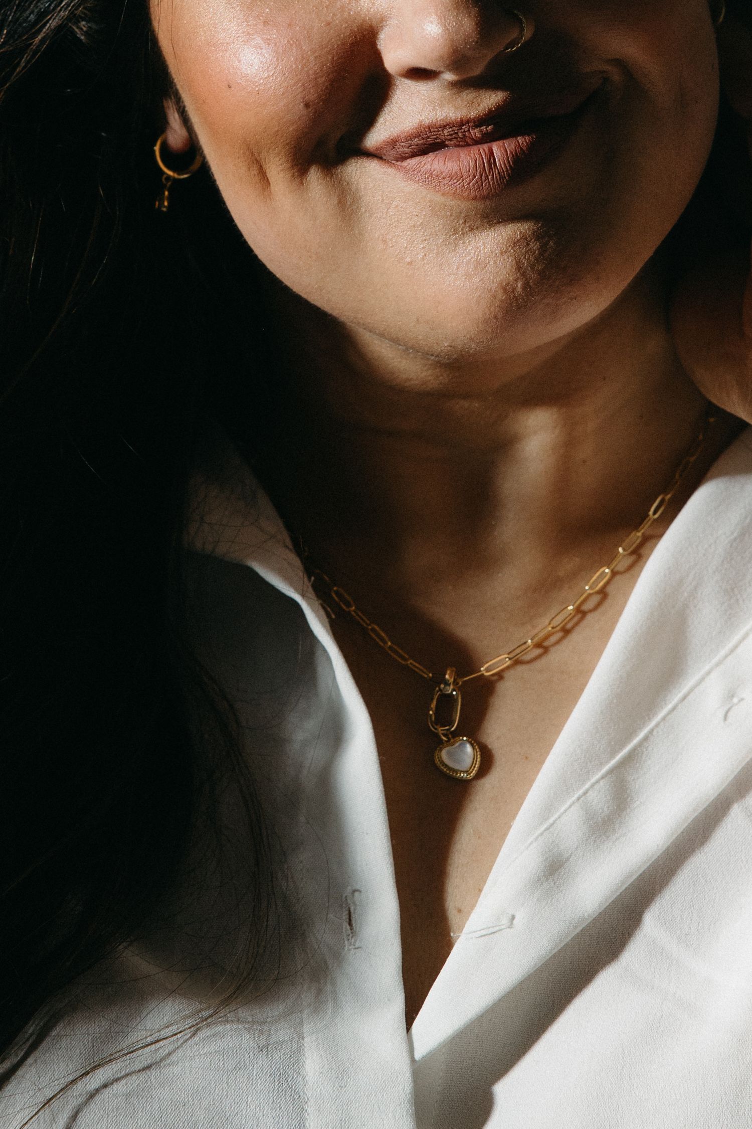 Close-up series of a gold chain necklace with pendant against a white shirt in dramatic lighting.
