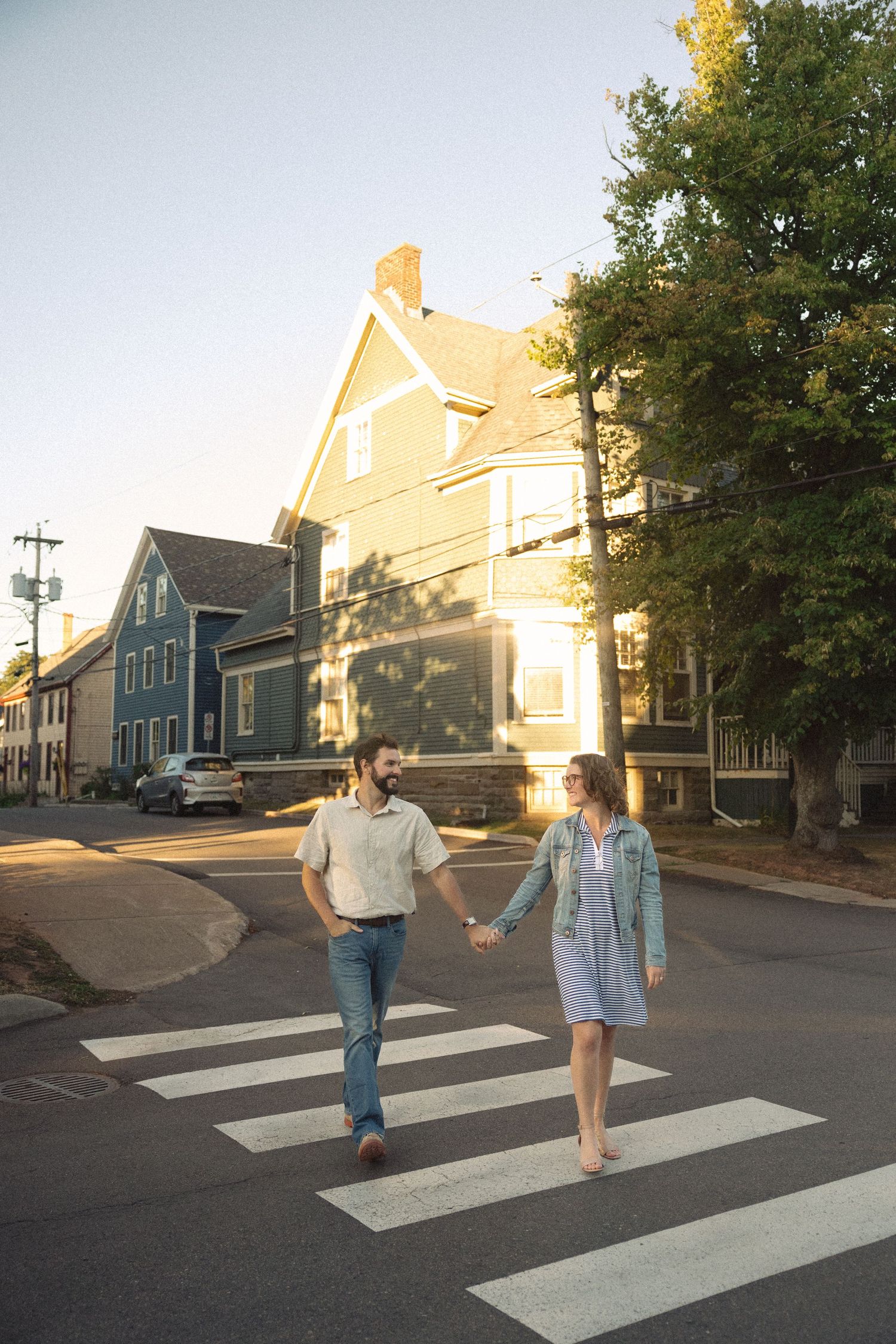 A couple walks across a crosswalk in a residential neighborhood during golden hour.