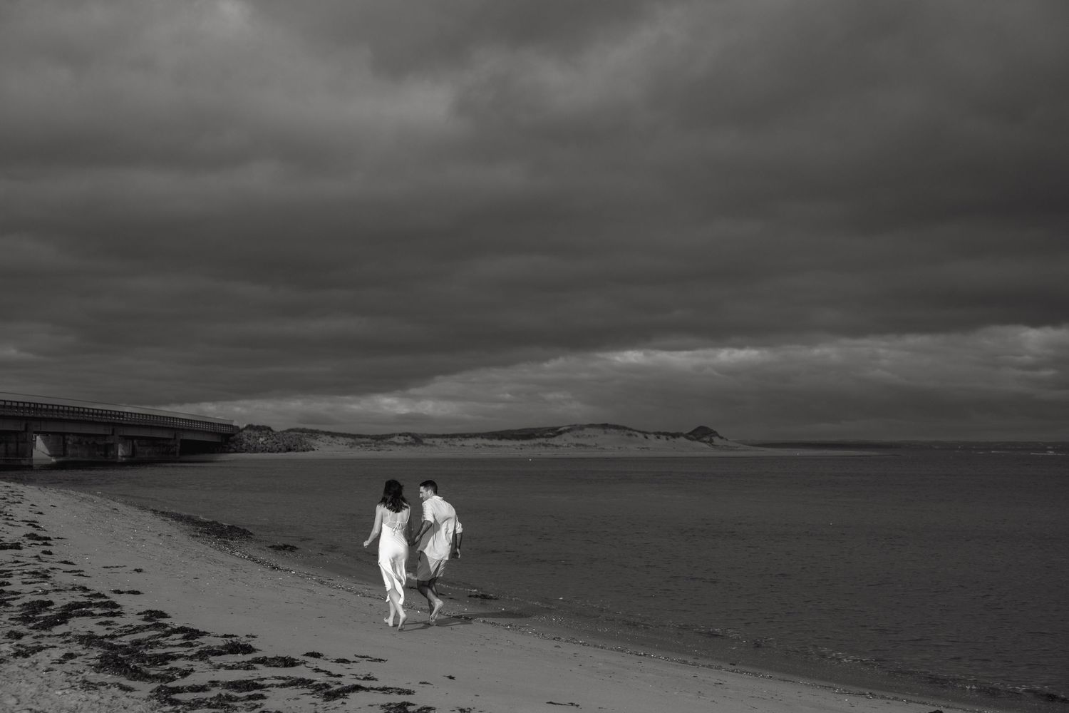 A black and white landscape photo of figures walking on a dramatic coastal beach.