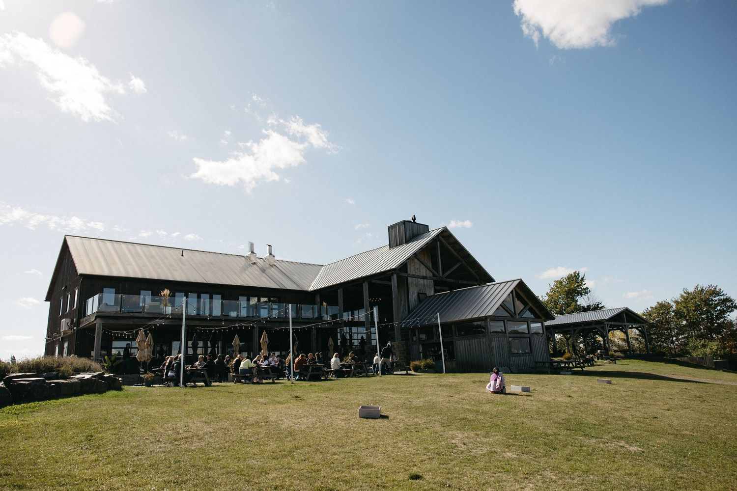 Panoramic view of a modern barn-style venue building against blue sky on a hilltop.