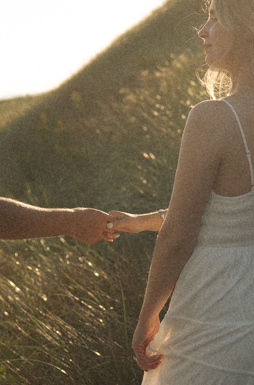 Couple holding hands in golden sunlight with green grassy hills in the background.