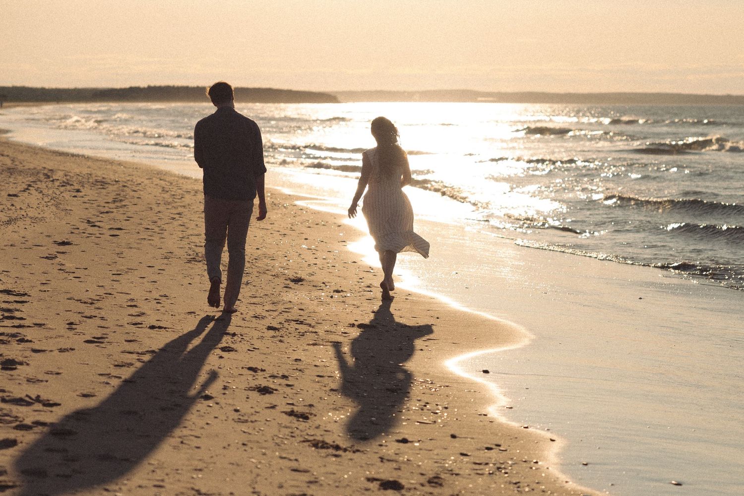 Couple walking hand in hand along a sandy beach at golden sunset.