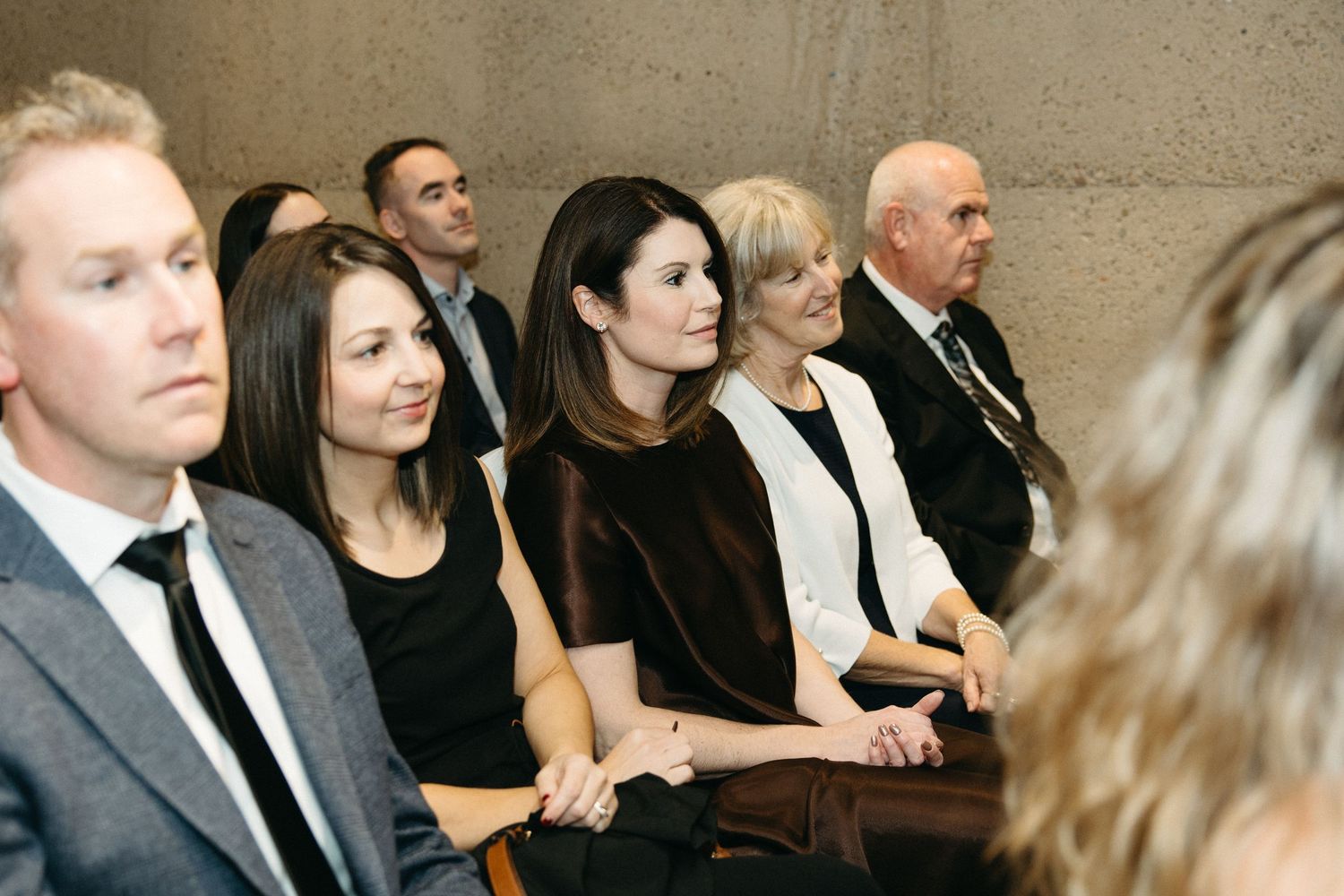 Wedding guests seated in formal attire watching a ceremony in an indoor venue.