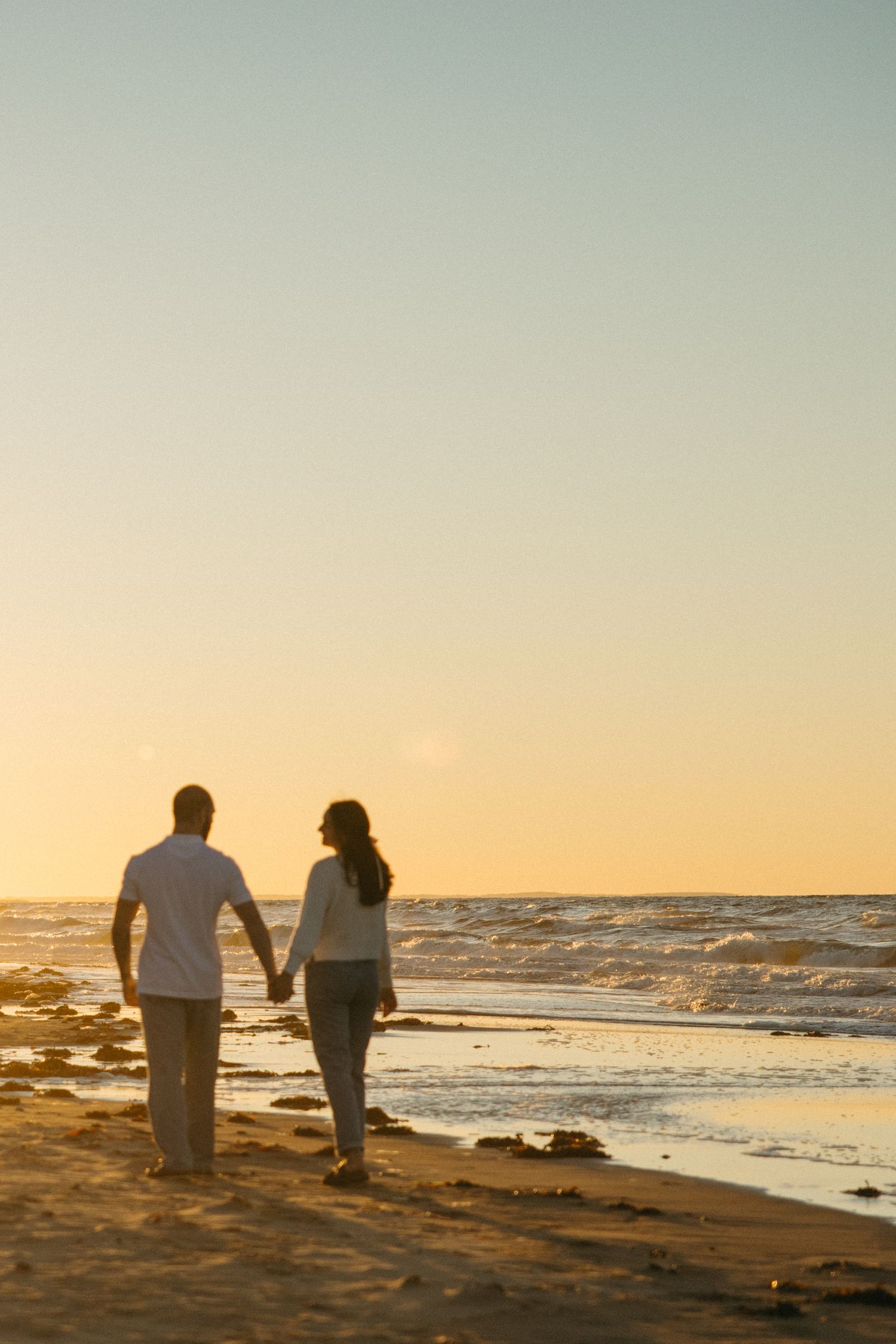 Silhouetted figures walking along rocky beach shore at sunset.