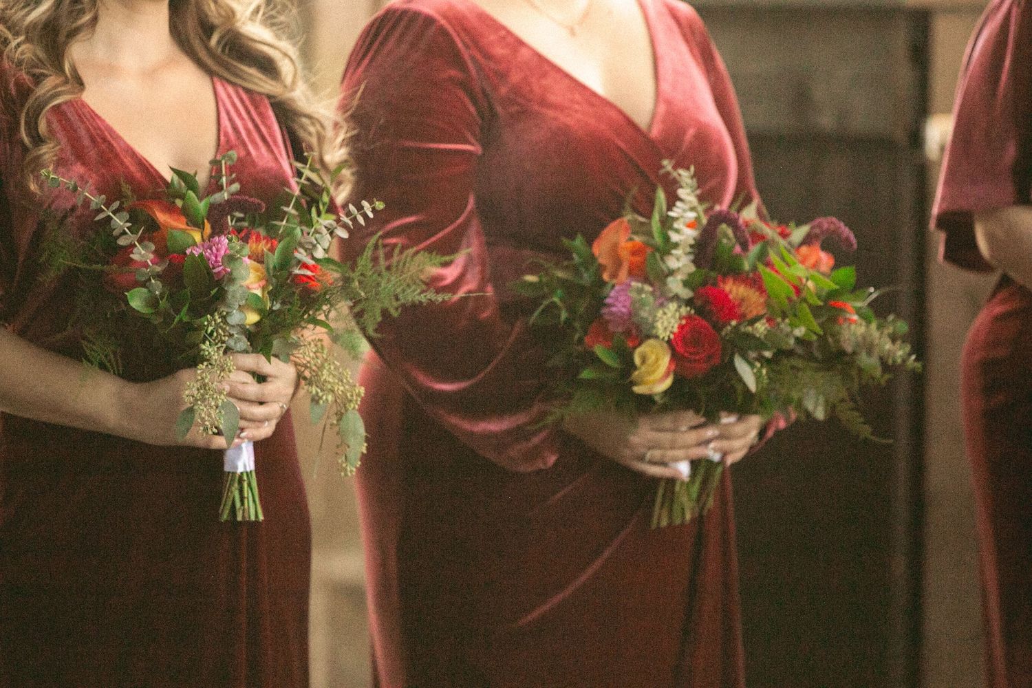 Row of burgundy bridesmaid dresses with floral bouquets.
