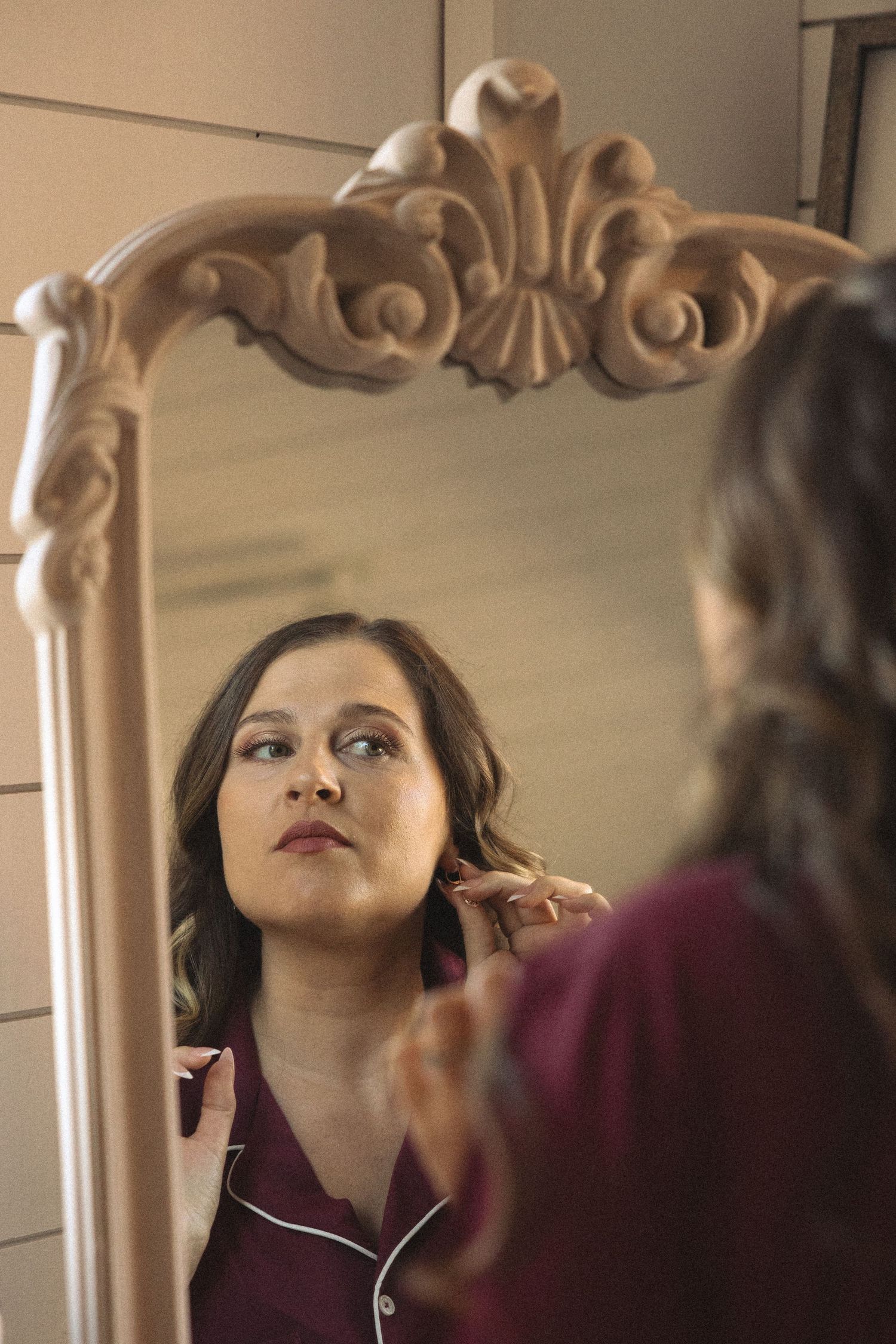 Person gazes into ornate mirror with carved details on beige wall.