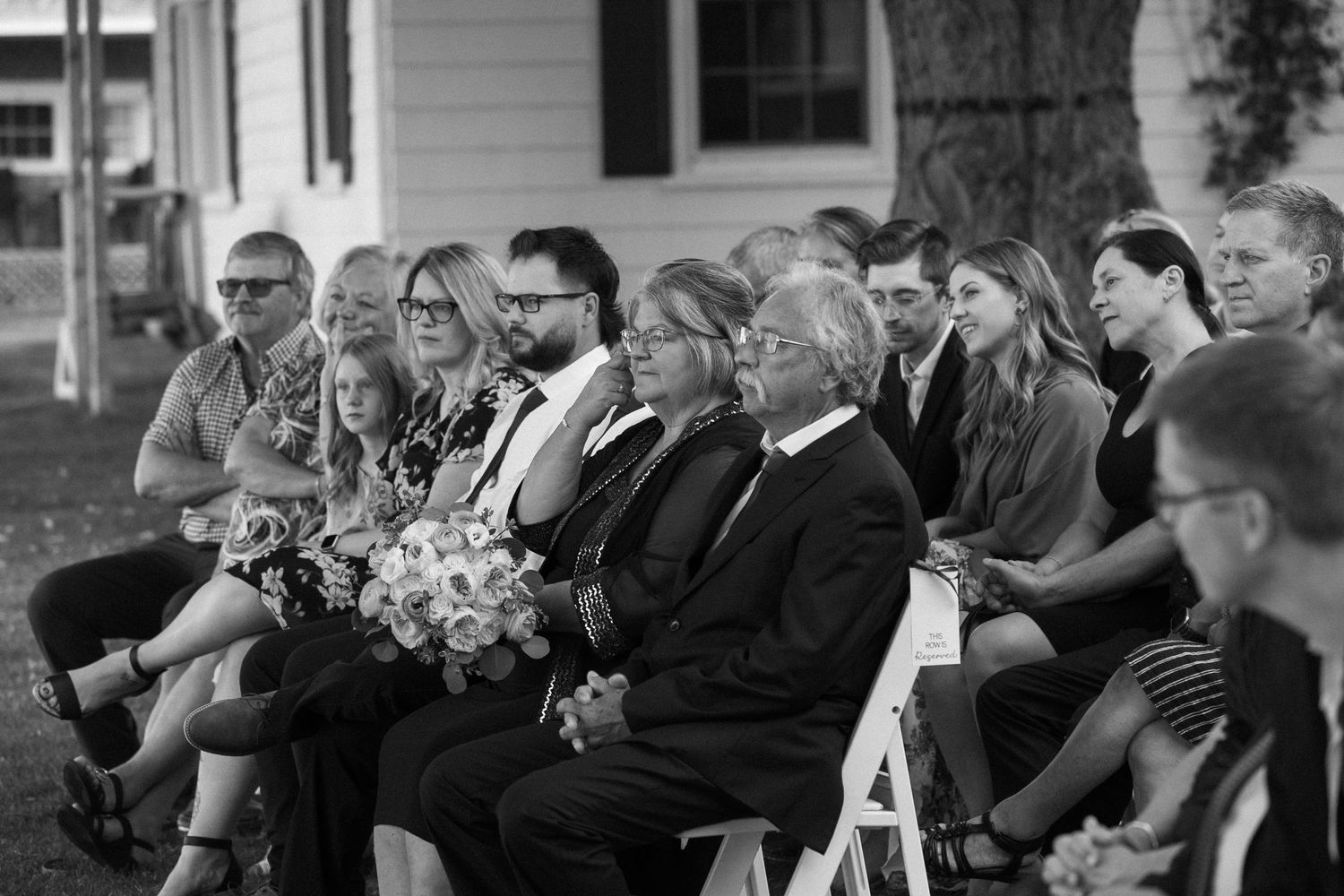 Black and white photo of wedding guests seated outdoors during a ceremony.