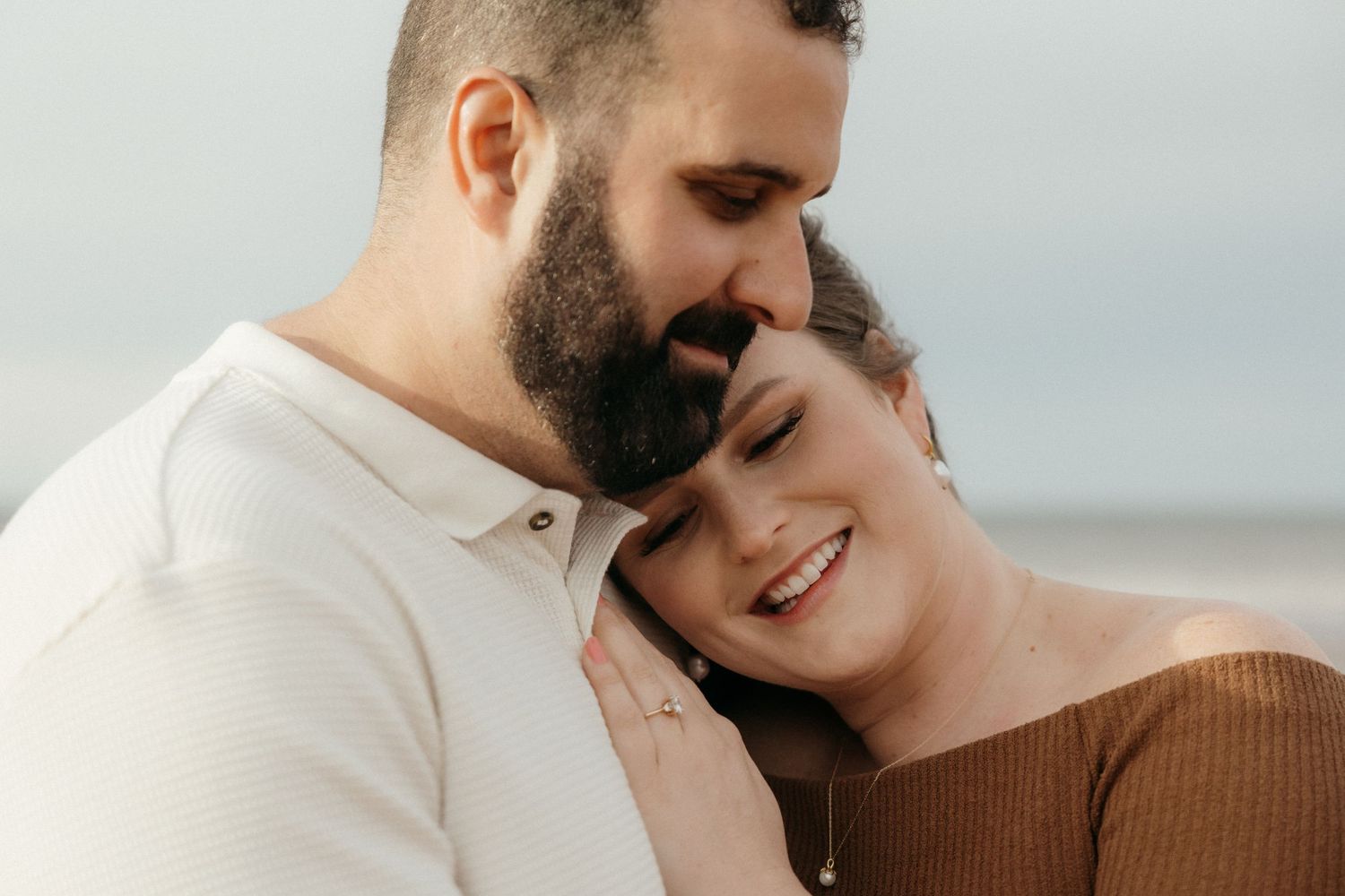 A romantic couple embraces while standing outdoors, with one wearing white and the other in brown.
