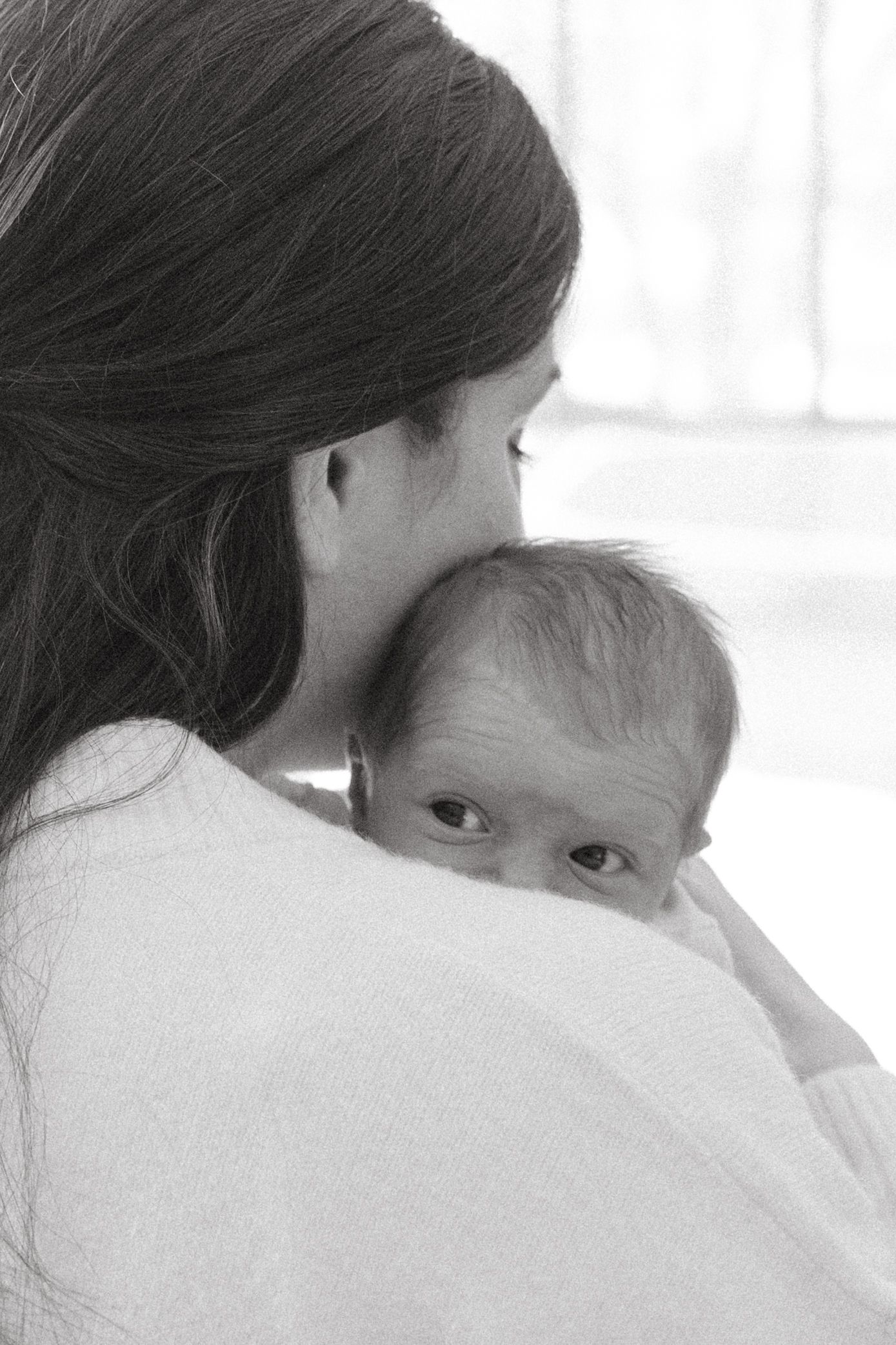 A tender black and white image shows a parent and baby in an intimate embrace against a light background.