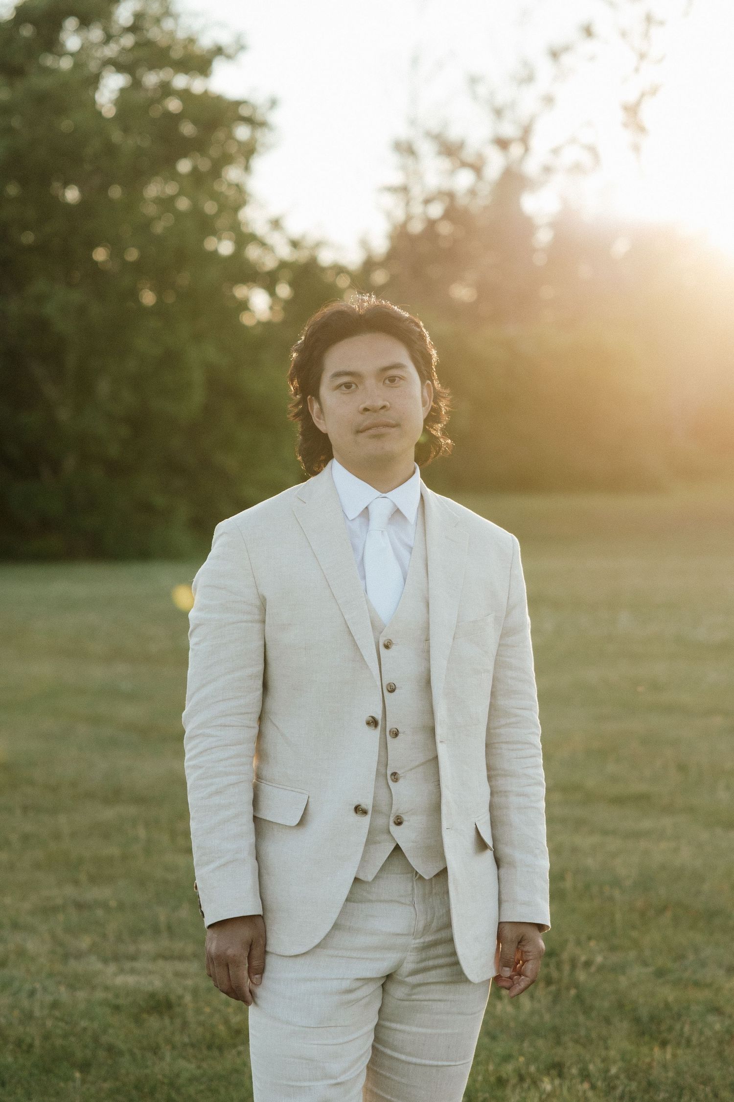 Groom in light colored three-piece suit poses during golden hour.