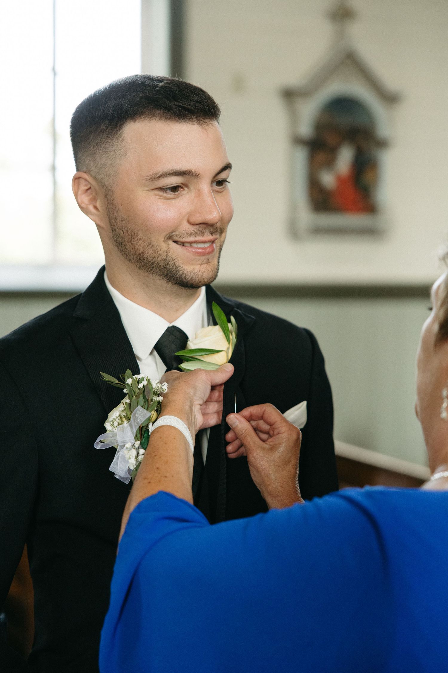 Groom gets his boutonniere pinned on by someone in a blue shirt.
