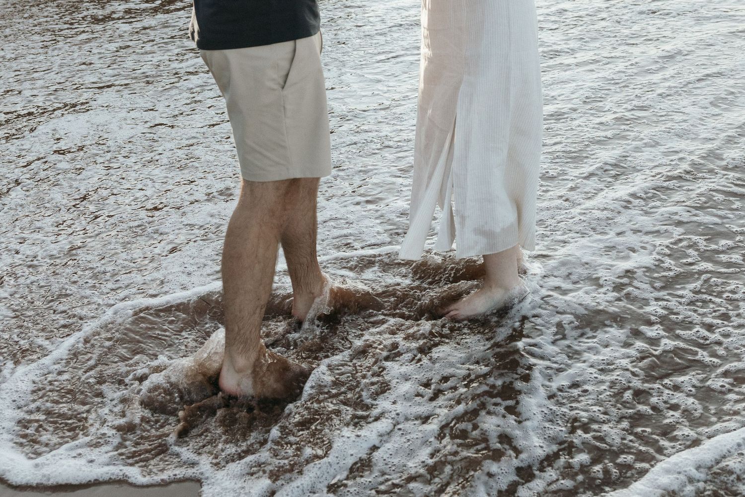 Bare feet in shallow ocean waves on a sandy beach.