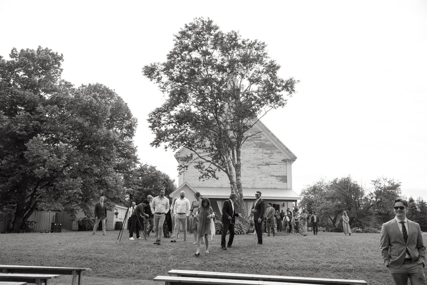 Black and white photo of wedding guests walking on lawn near historic white church building.