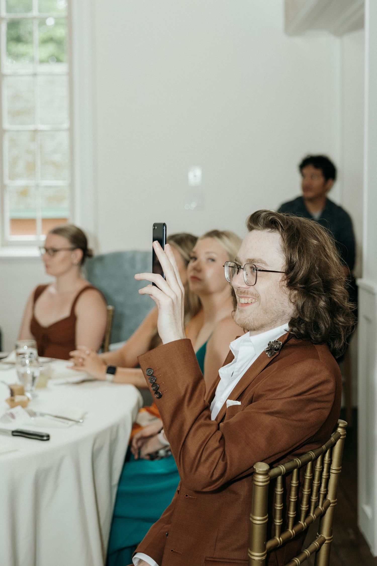 Wedding guests react emotionally while watching speeches at elegant indoor reception.
