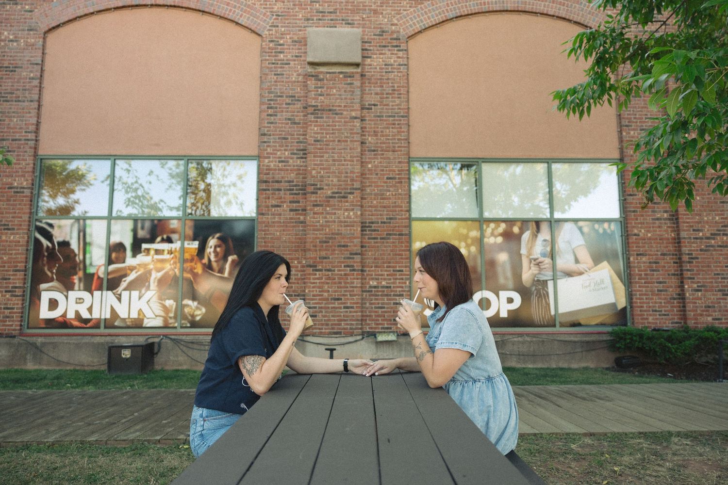 Two people sitting across from each other at a black outdoor table near a brick storefront.