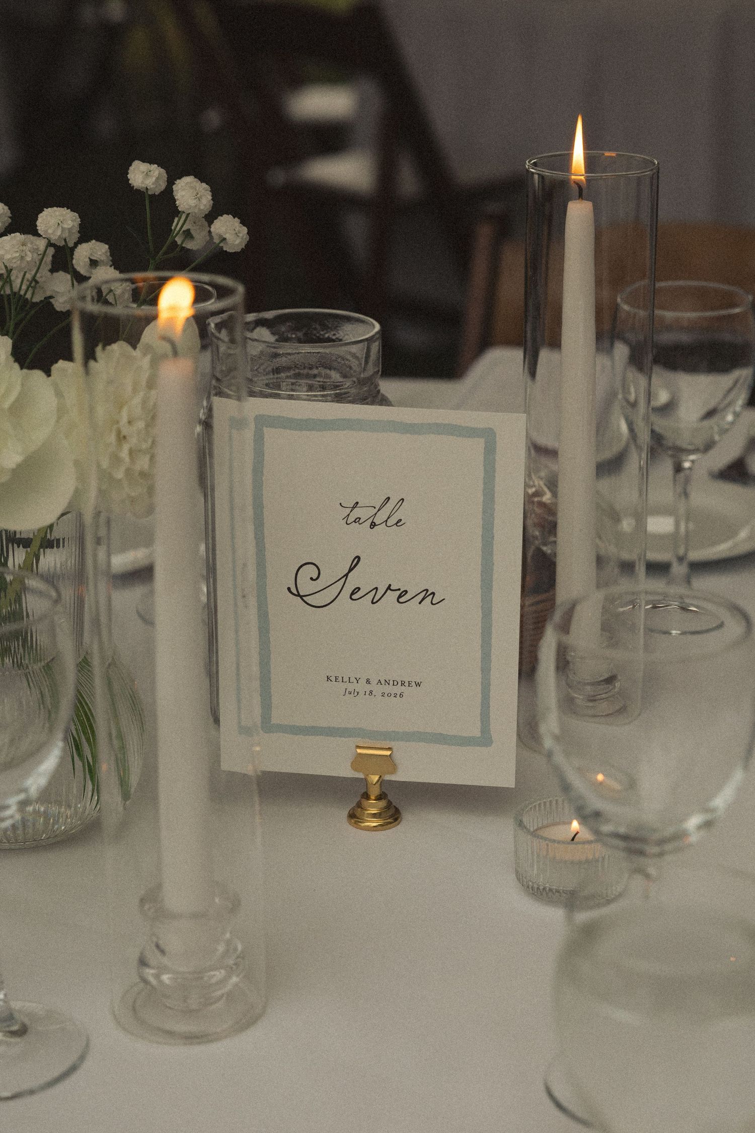 Elegant wedding table seven place card with lit candles and white floral centerpiece.