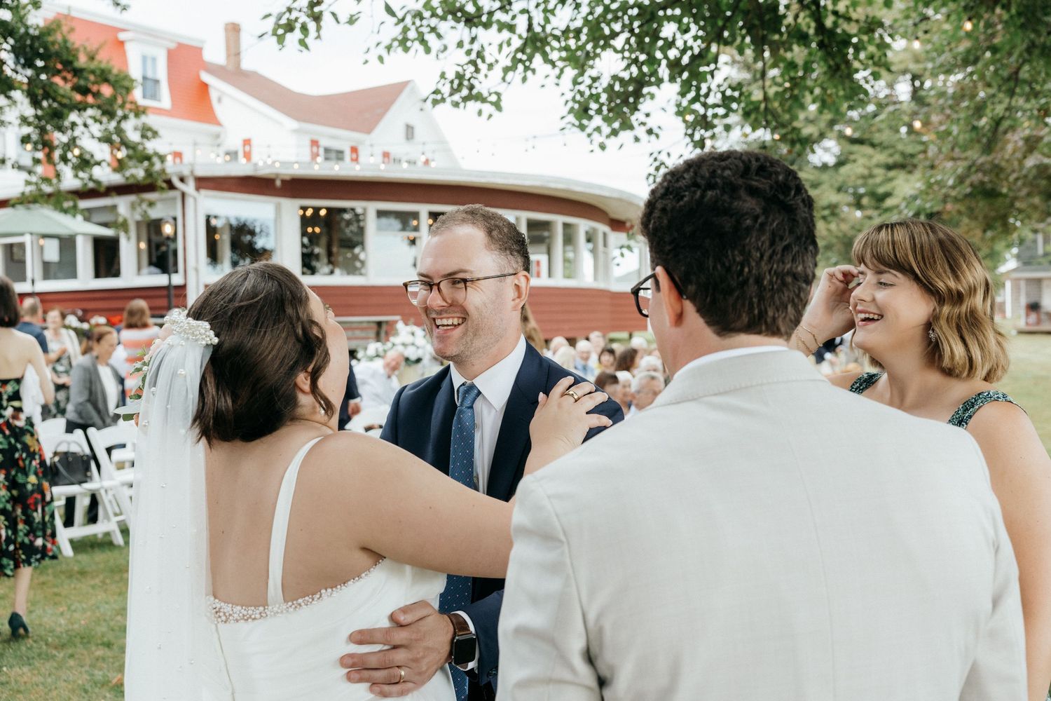 Wedding guests laughing and embracing newlyweds outdoors after ceremony.