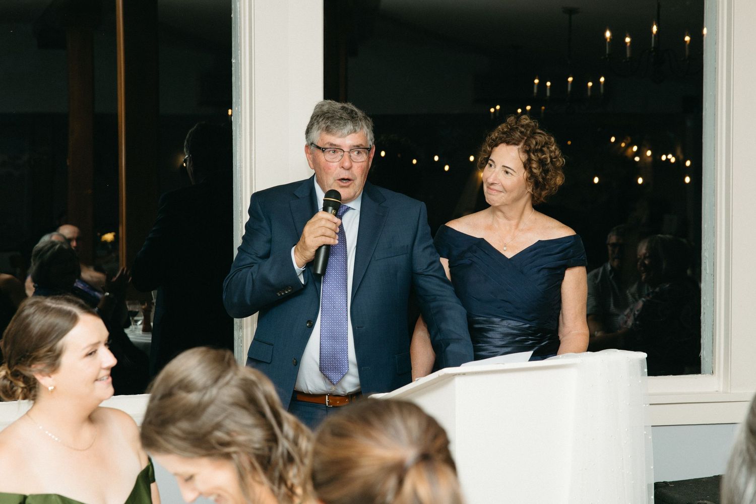 Couple gives wedding reception speech at podium with microphone in elegant indoor venue.