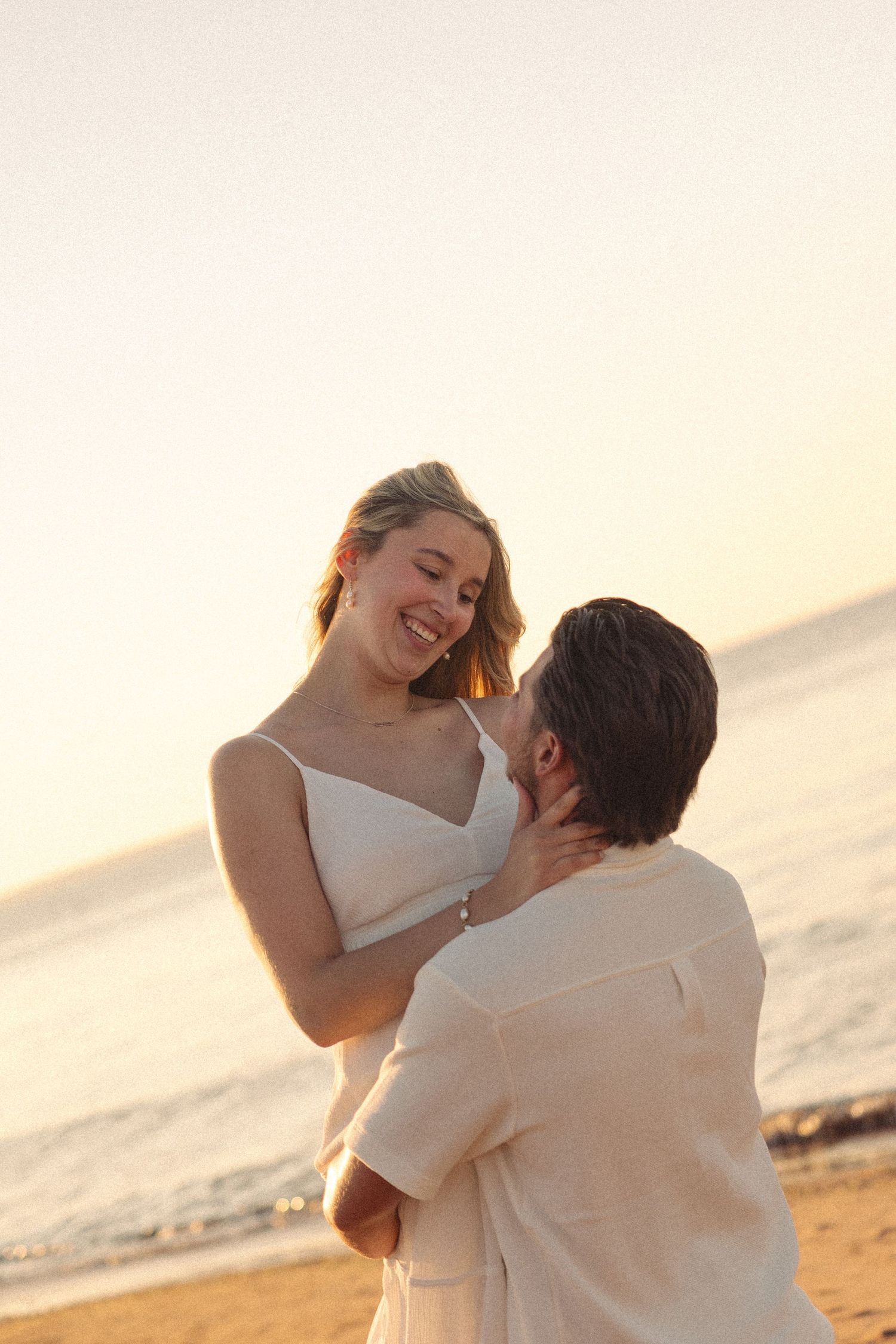 Happy couple embracing and laughing together on a sandy beach at golden sunset.