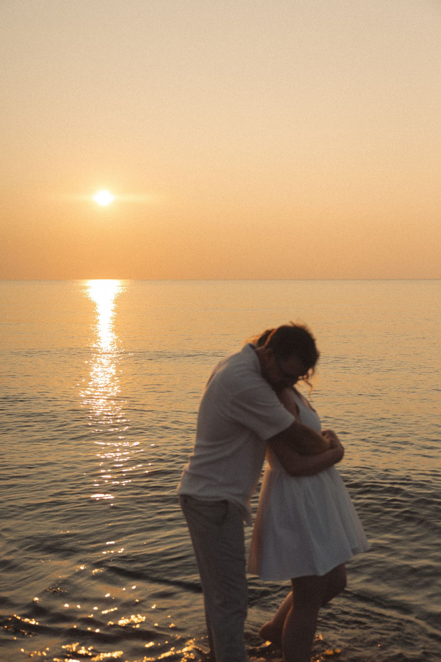 Couple sharing tender embrace silhouetted against golden ocean sunset on beach.