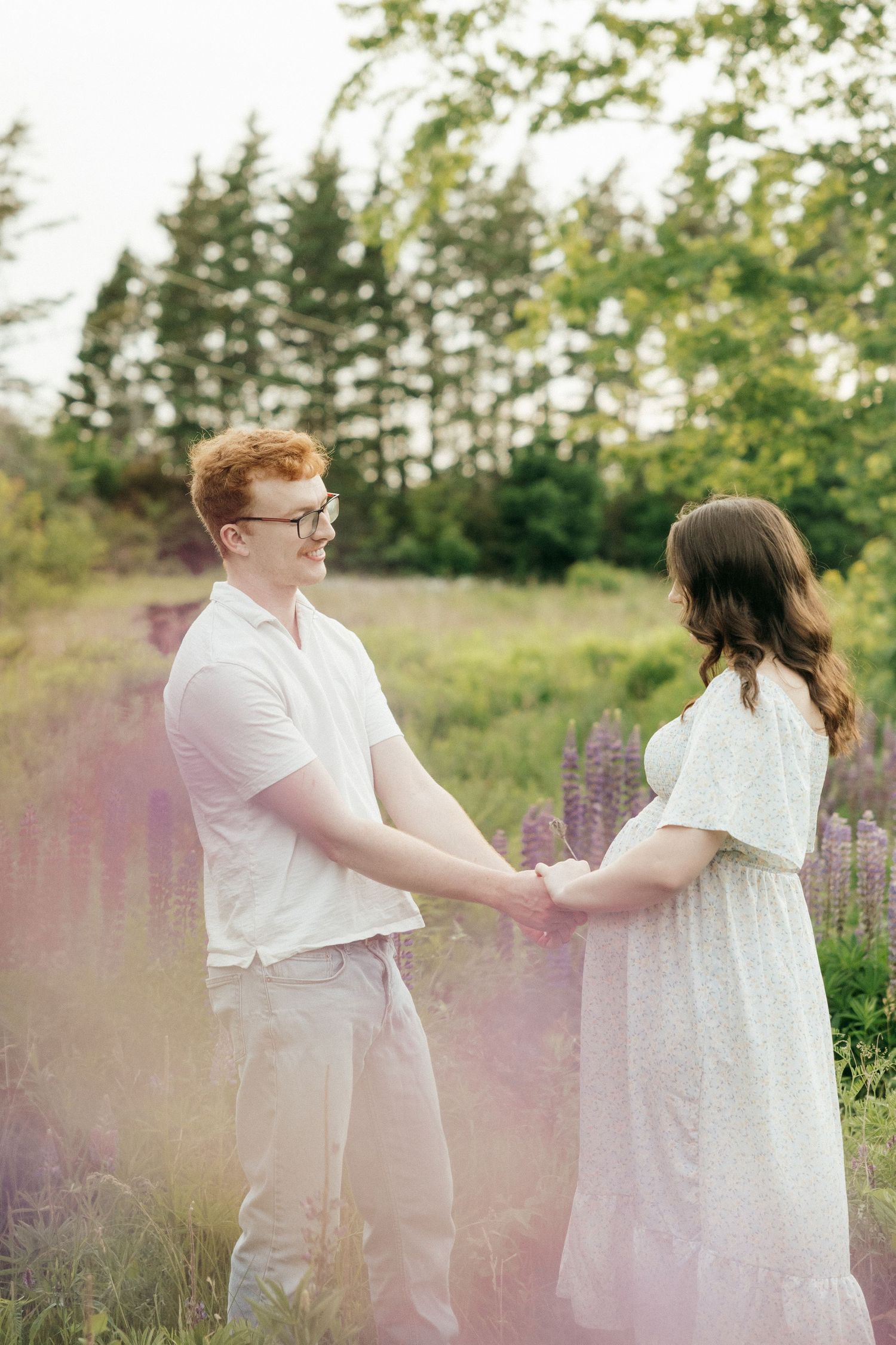A couple dances together in a dreamy meadow filled with purple wildflowers and soft sunlight.