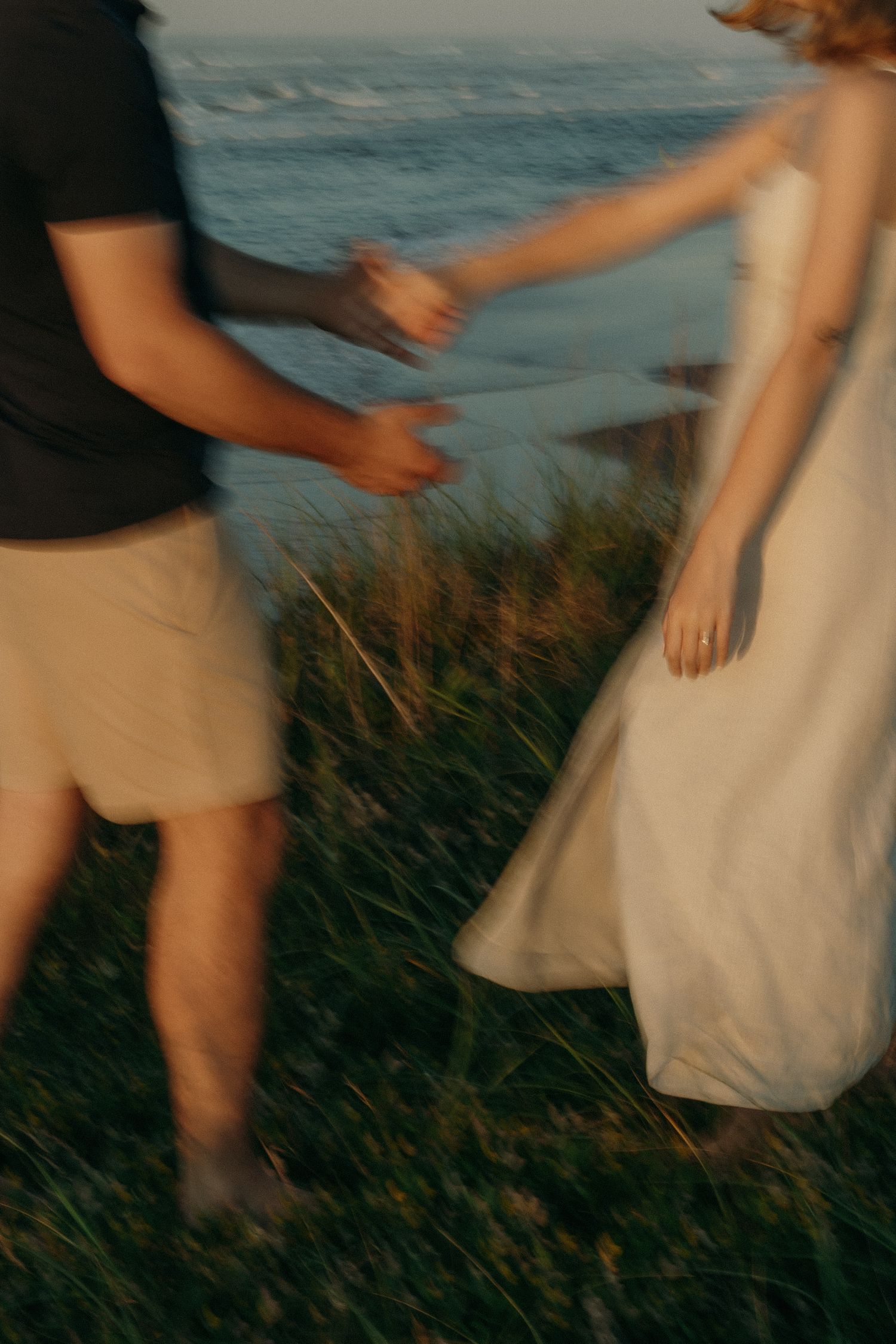 Motion-blurred image of hands clasped together against coastal grass and ocean backdrop.