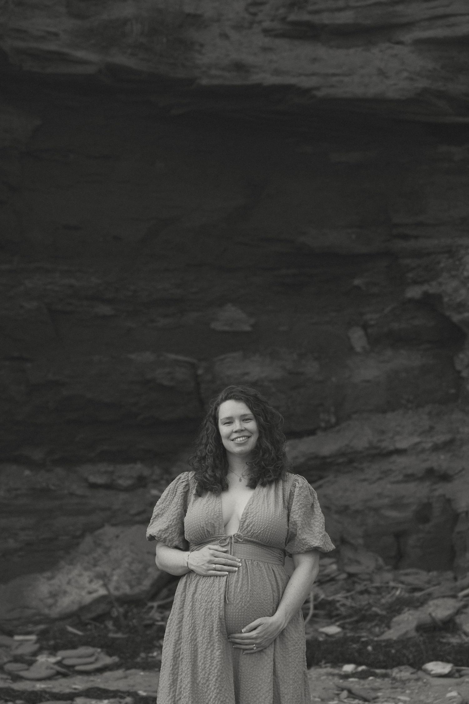 Black and white maternity portrait with natural rock formations in the background.