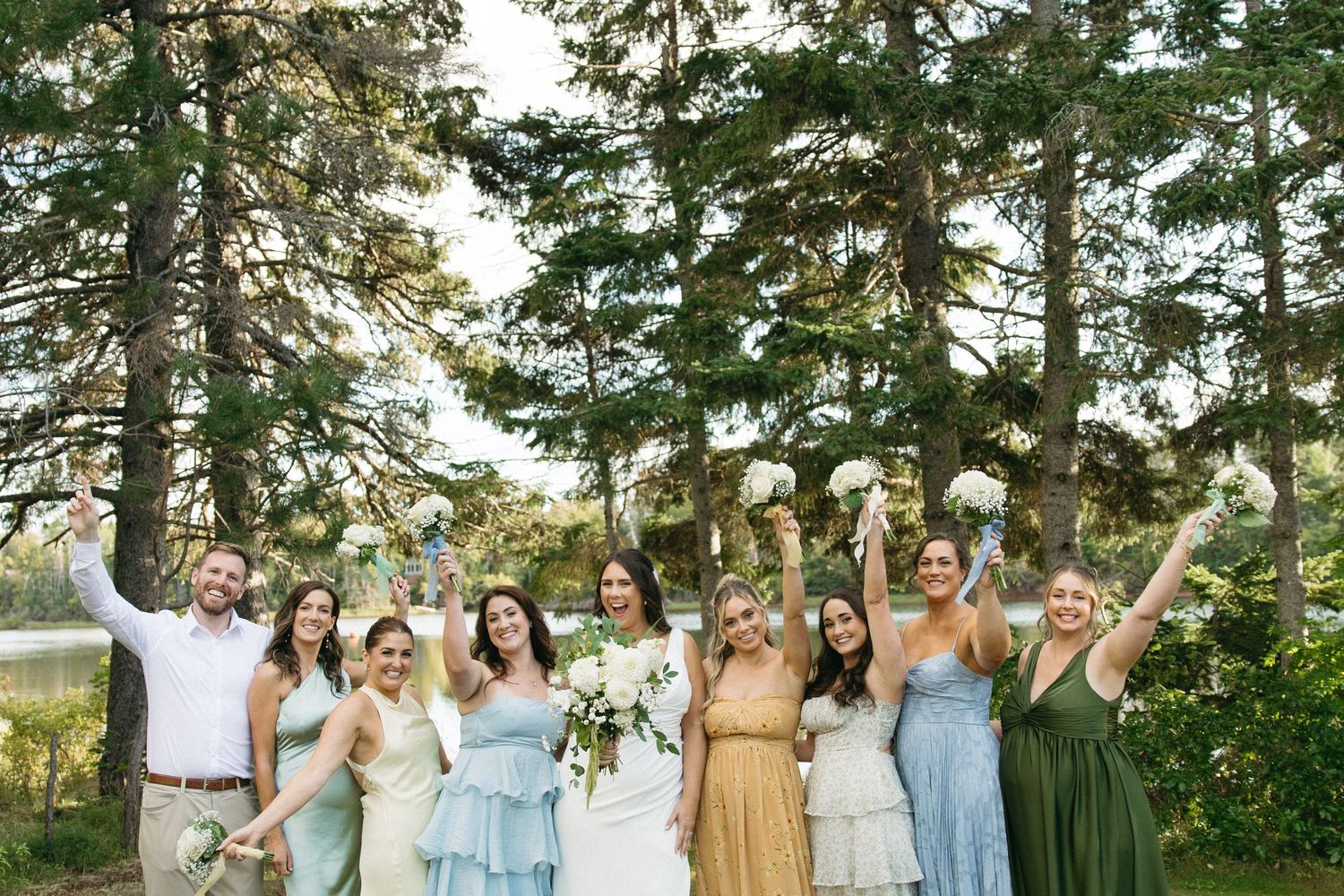 Wedding party in pastel dresses posing together under tall pine trees.