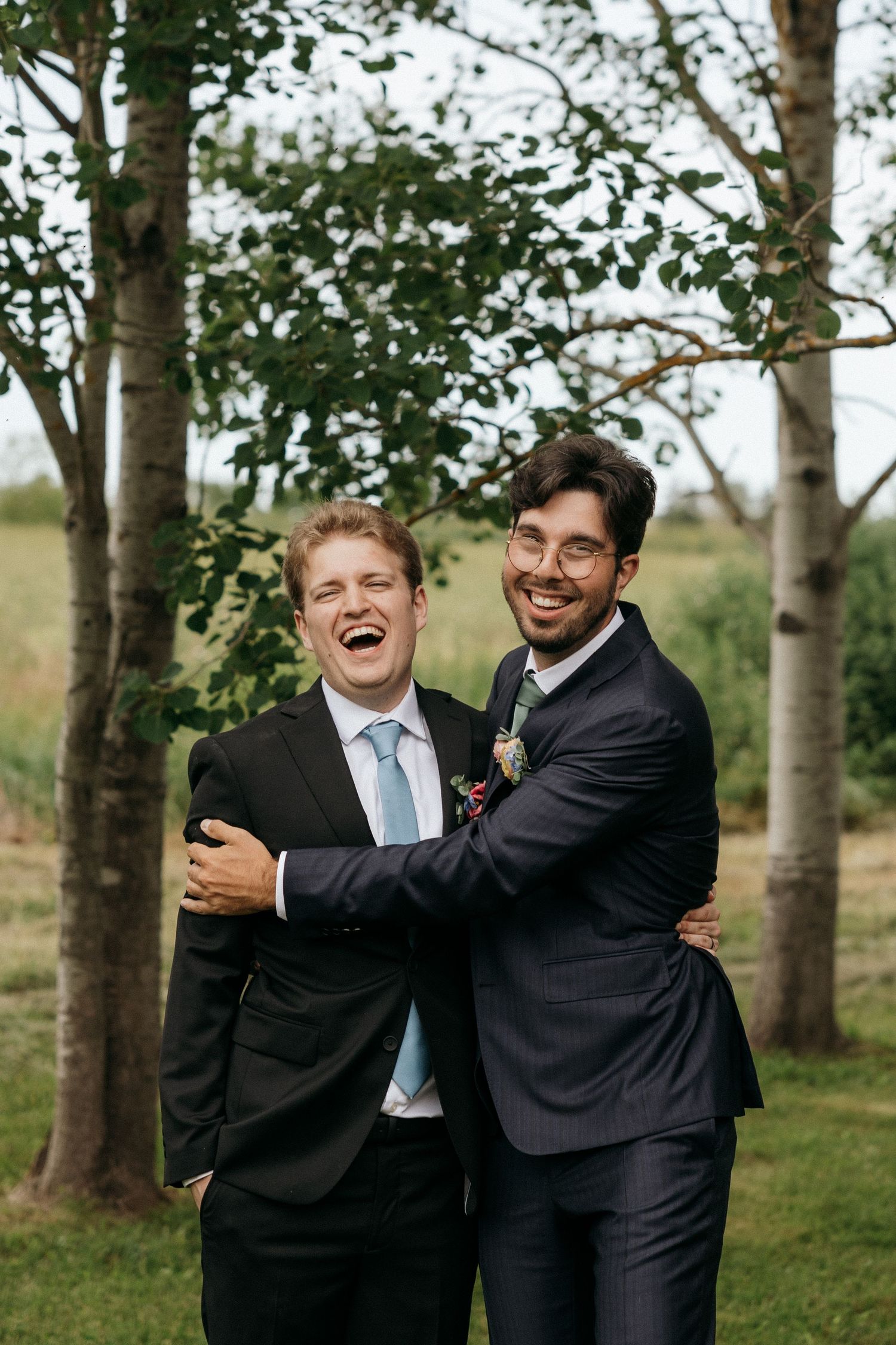 Groomsmen sharing laughs and hugs in a wooded outdoor setting.