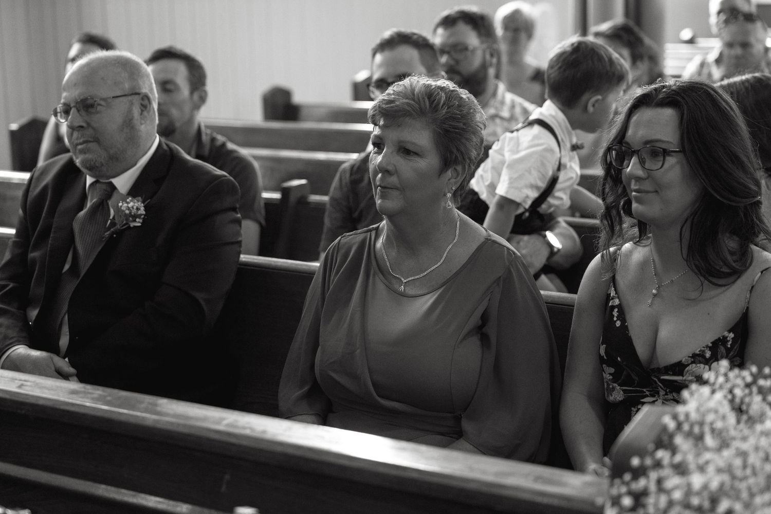 Black and white photo of wedding guests seated in church pews watching the ceremony.