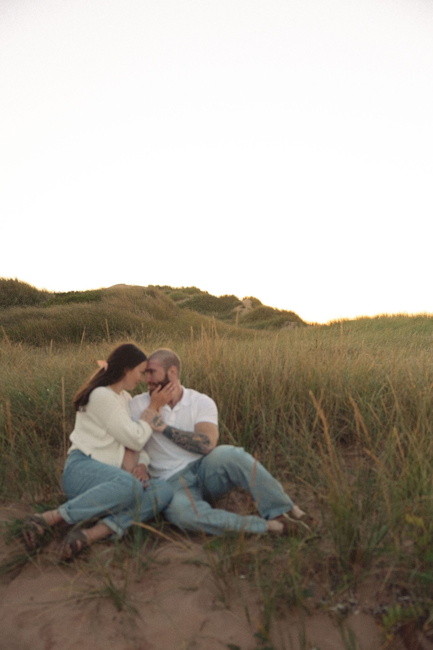 Couple relaxing together on grassy sand dunes at sunset.