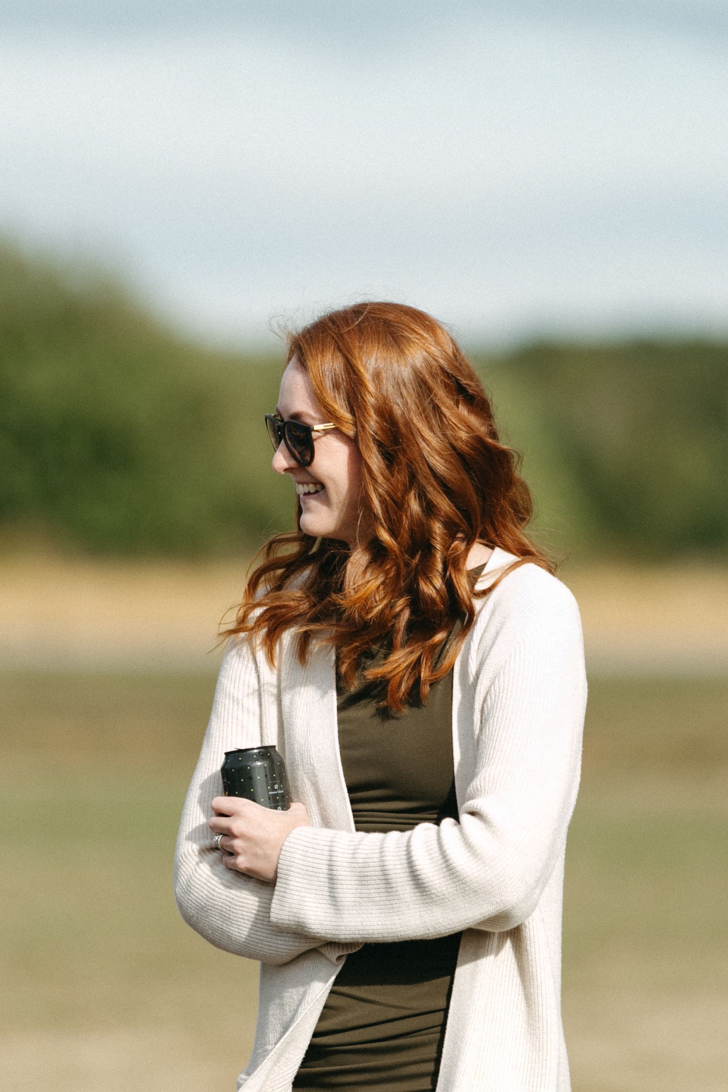 Person in white sweater laughs joyfully outdoors on a sunny day.