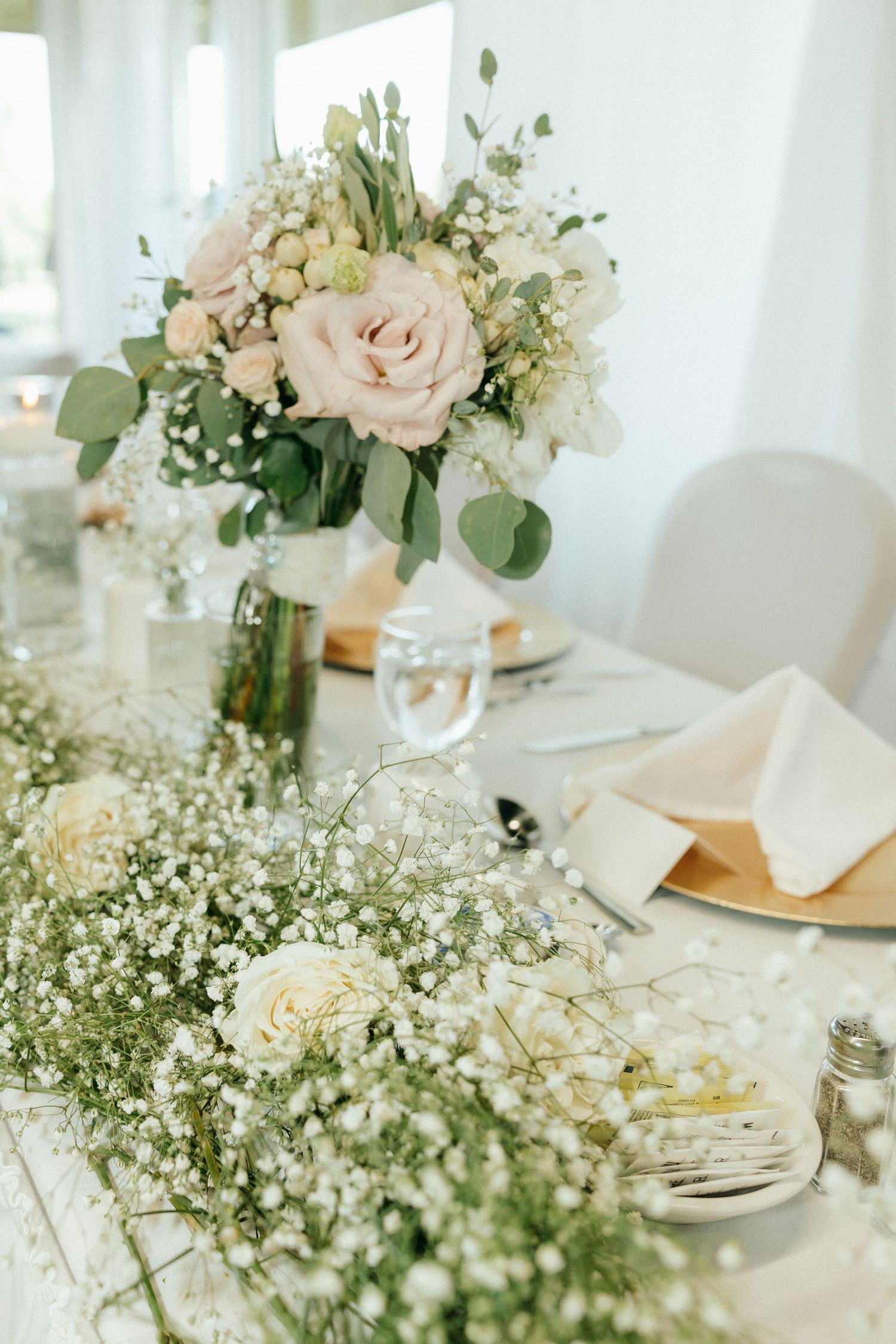 Elegant wedding reception table settings with white roses and baby's breath centerpieces.