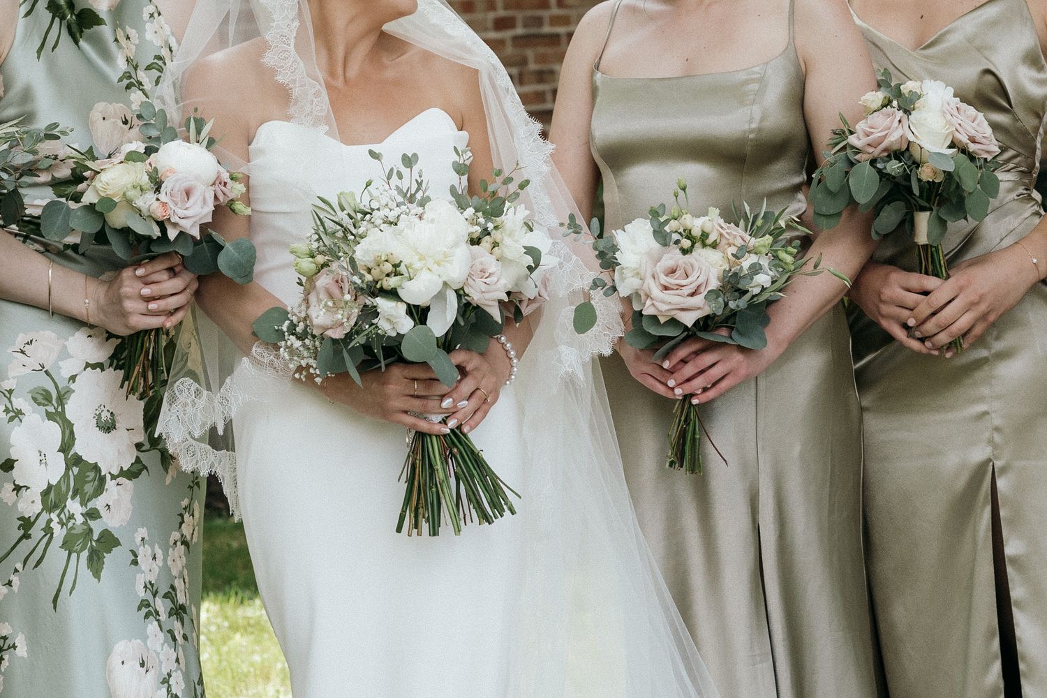 Wedding party members hold elegant white floral bouquets while standing in a row.