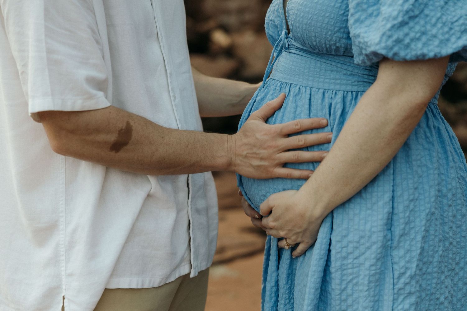 A couple in blue and white outfits share an intimate moment against a rocky beach backdrop.