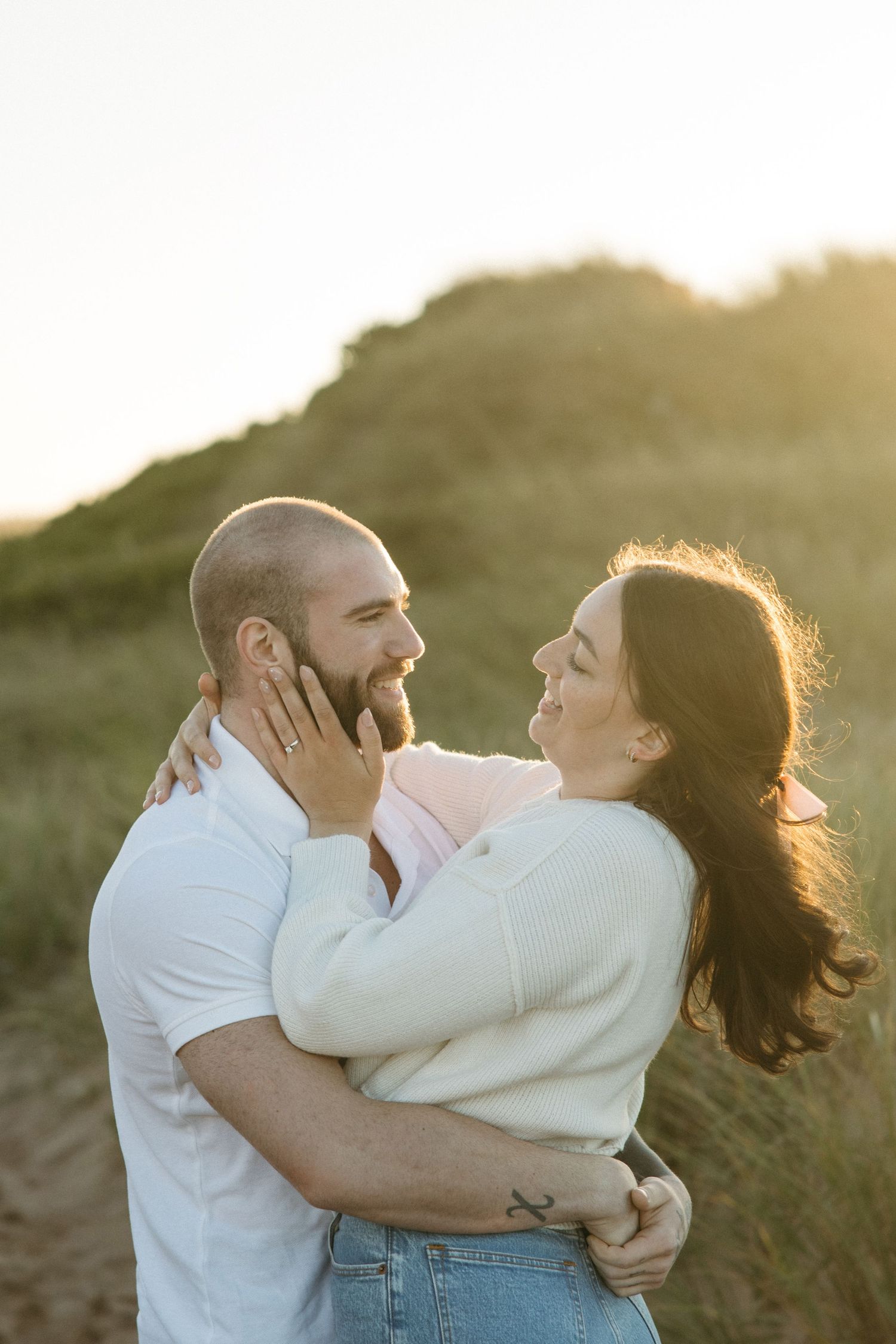 Couple sharing loving embrace against golden sunset on beach dunes.