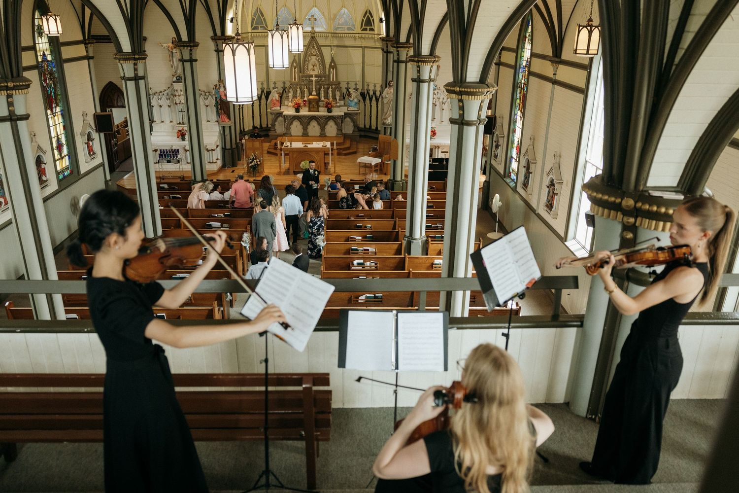 Musicians perform in an ornate church with gothic arches and wooden pews.