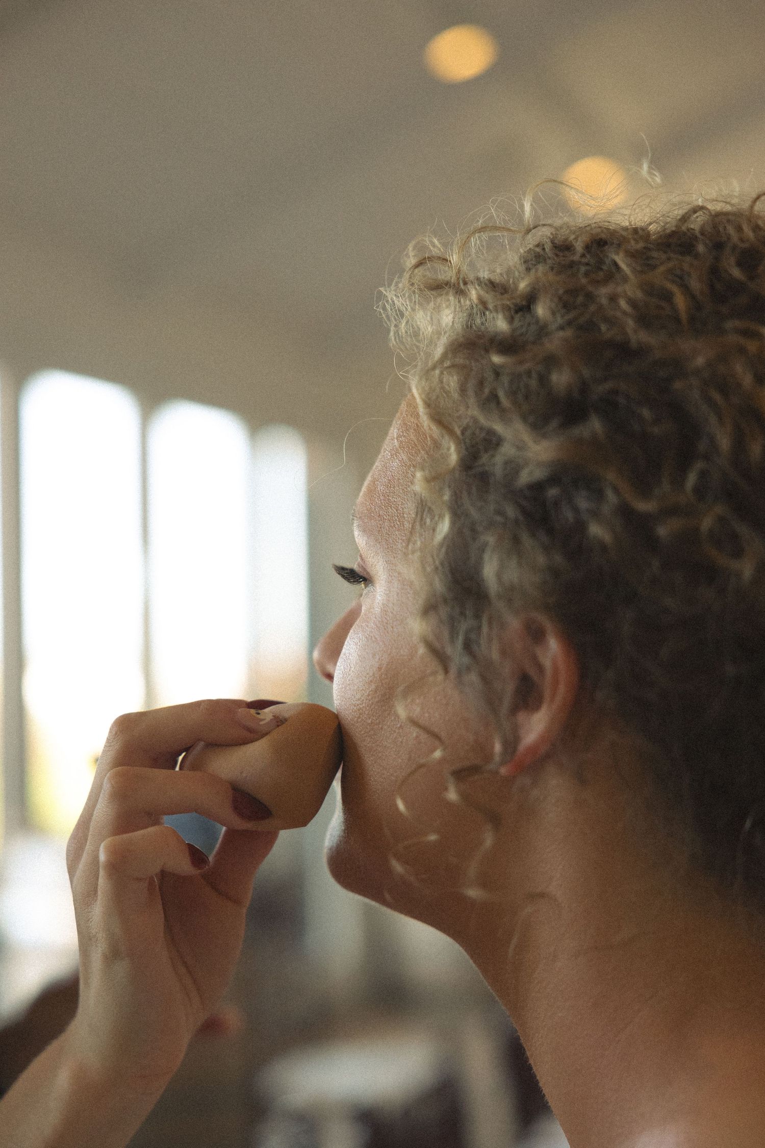 Side profile of someone applying makeup in soft lighting.